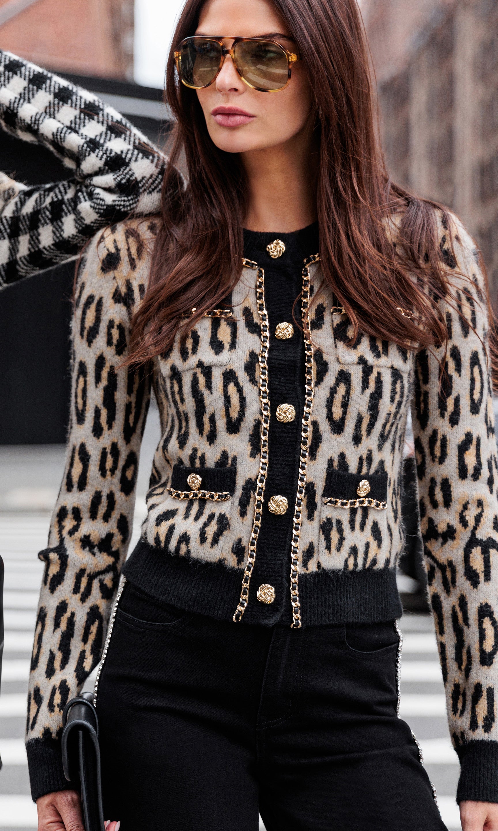 Woman wearing a leopard print cardigan with gold buttons and chain on a city street.