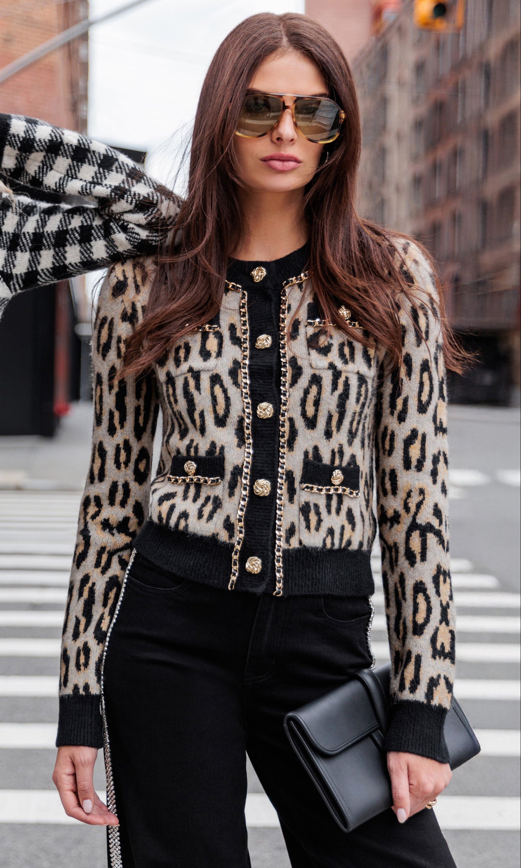 Woman wearing a leopard print cardigan with a cityscape design, standing on a crosswalk.