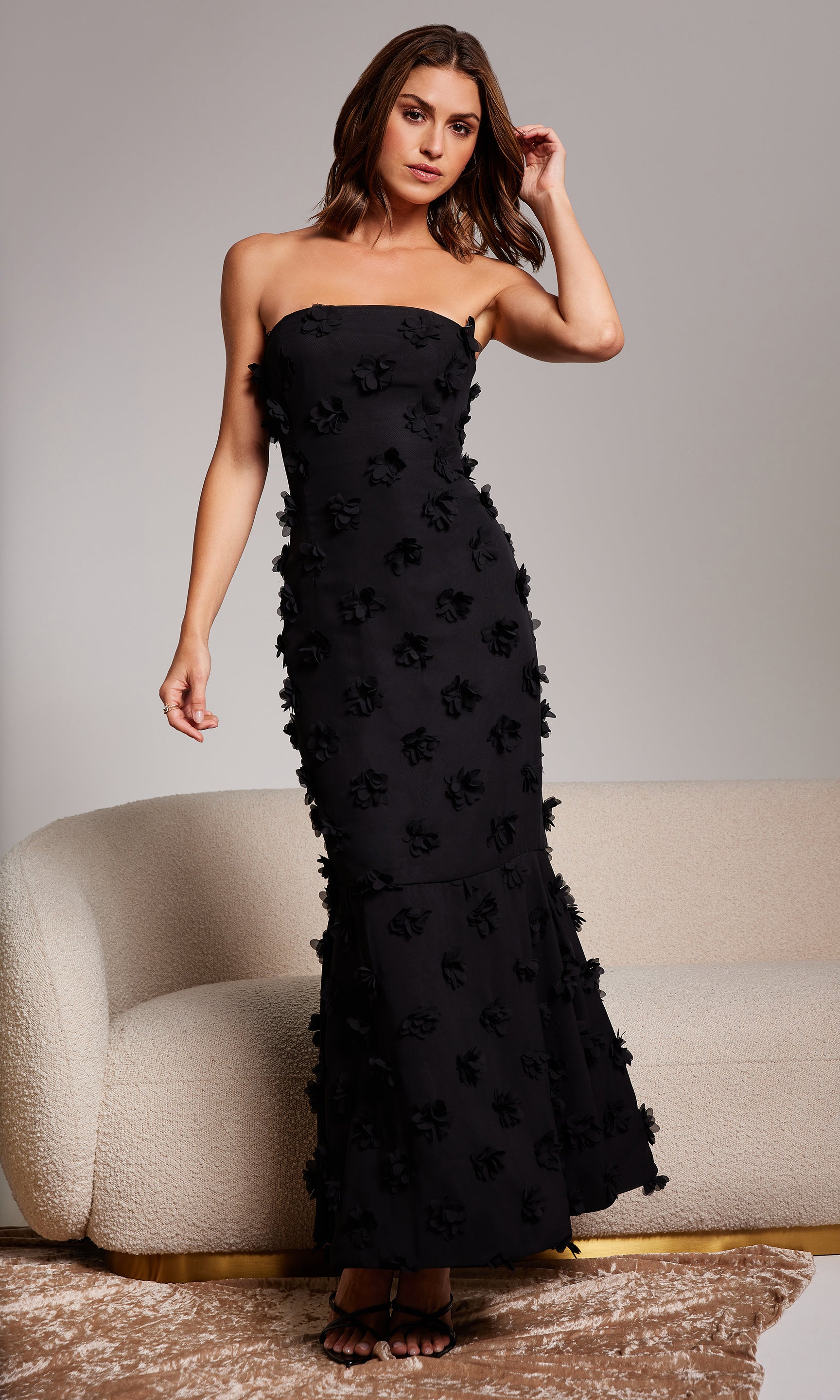 Woman wearing a black strapless gown with floral details against a neutral background