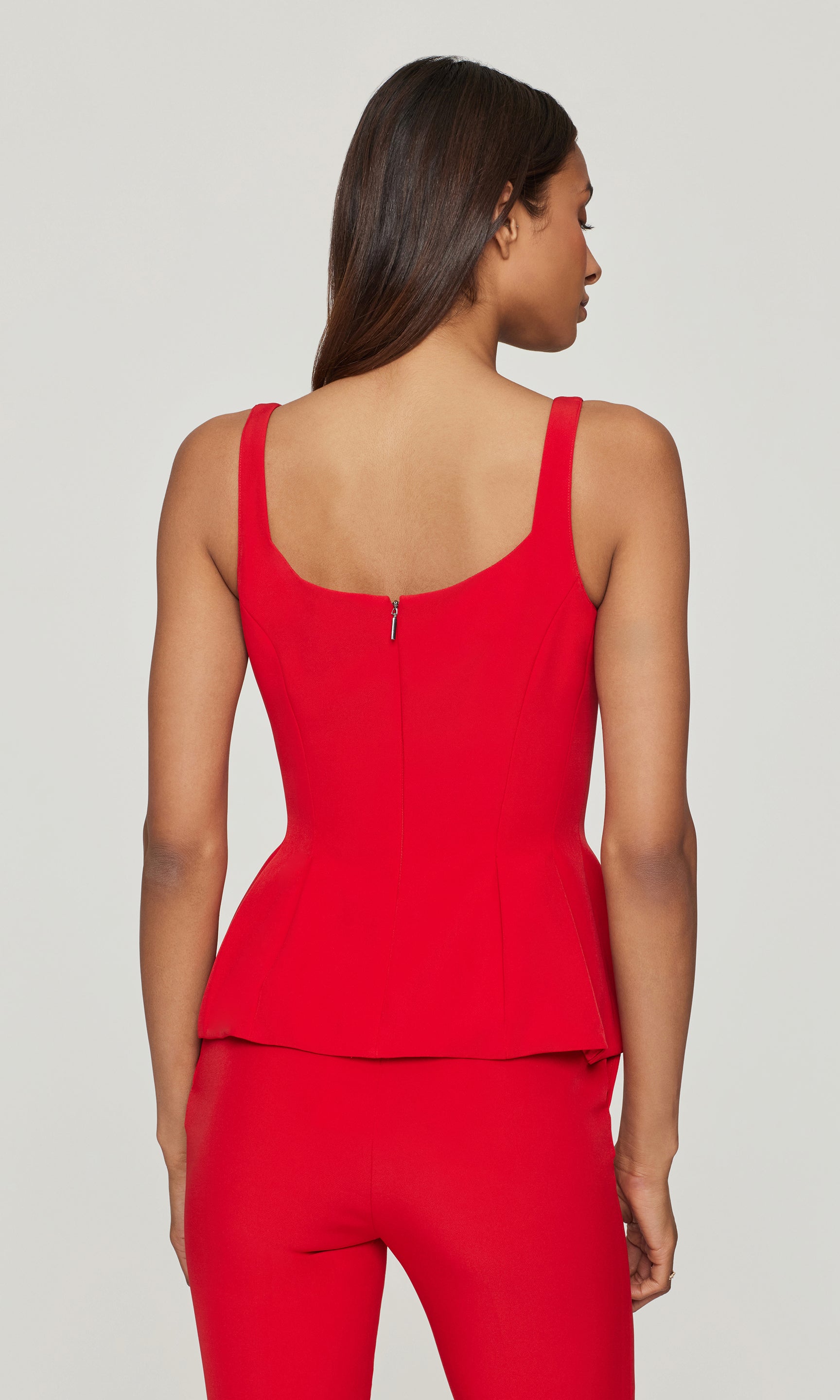 Back view of woman wearing a red peplum top and pants on a plain background