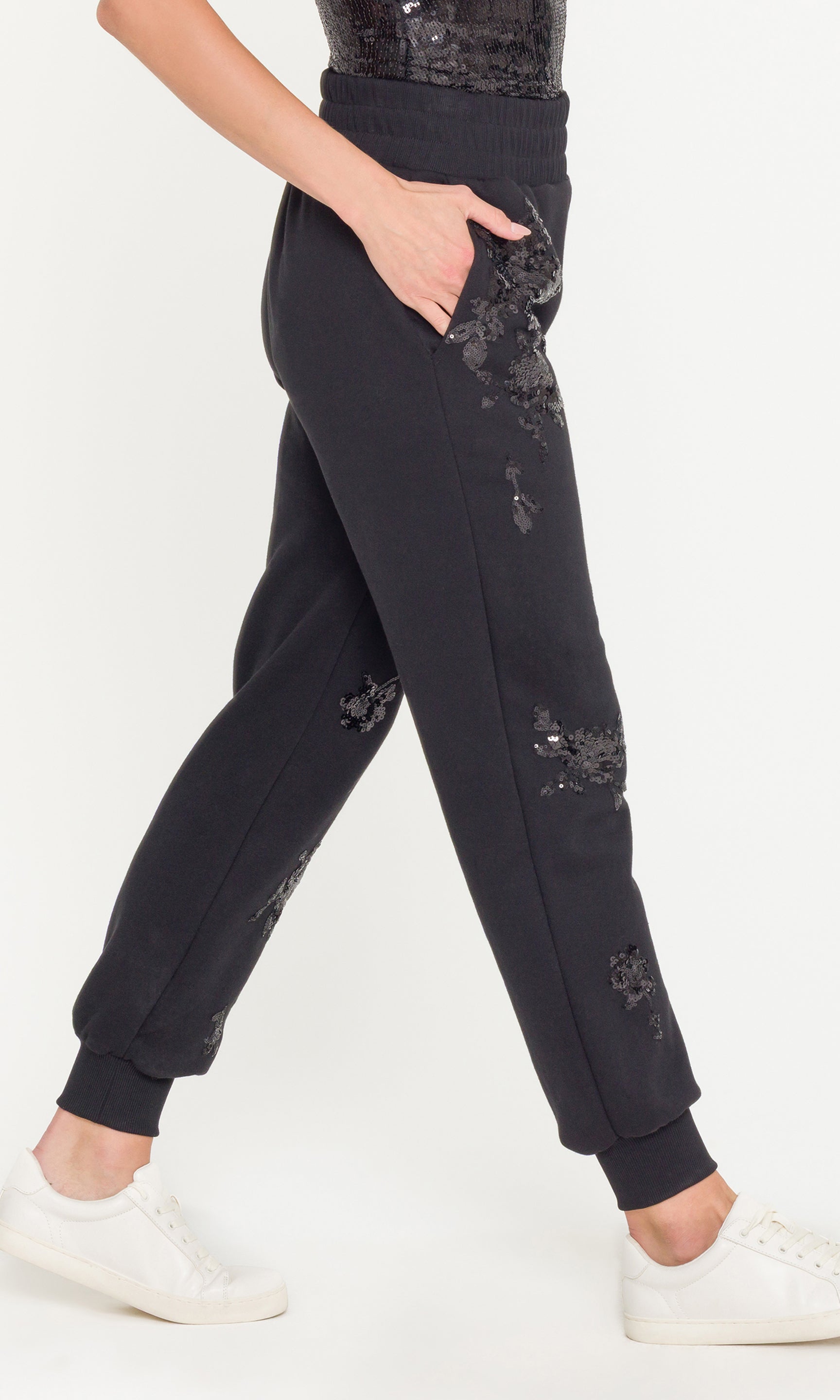 Black sequin adorned jogger pants worn by a person on a white background