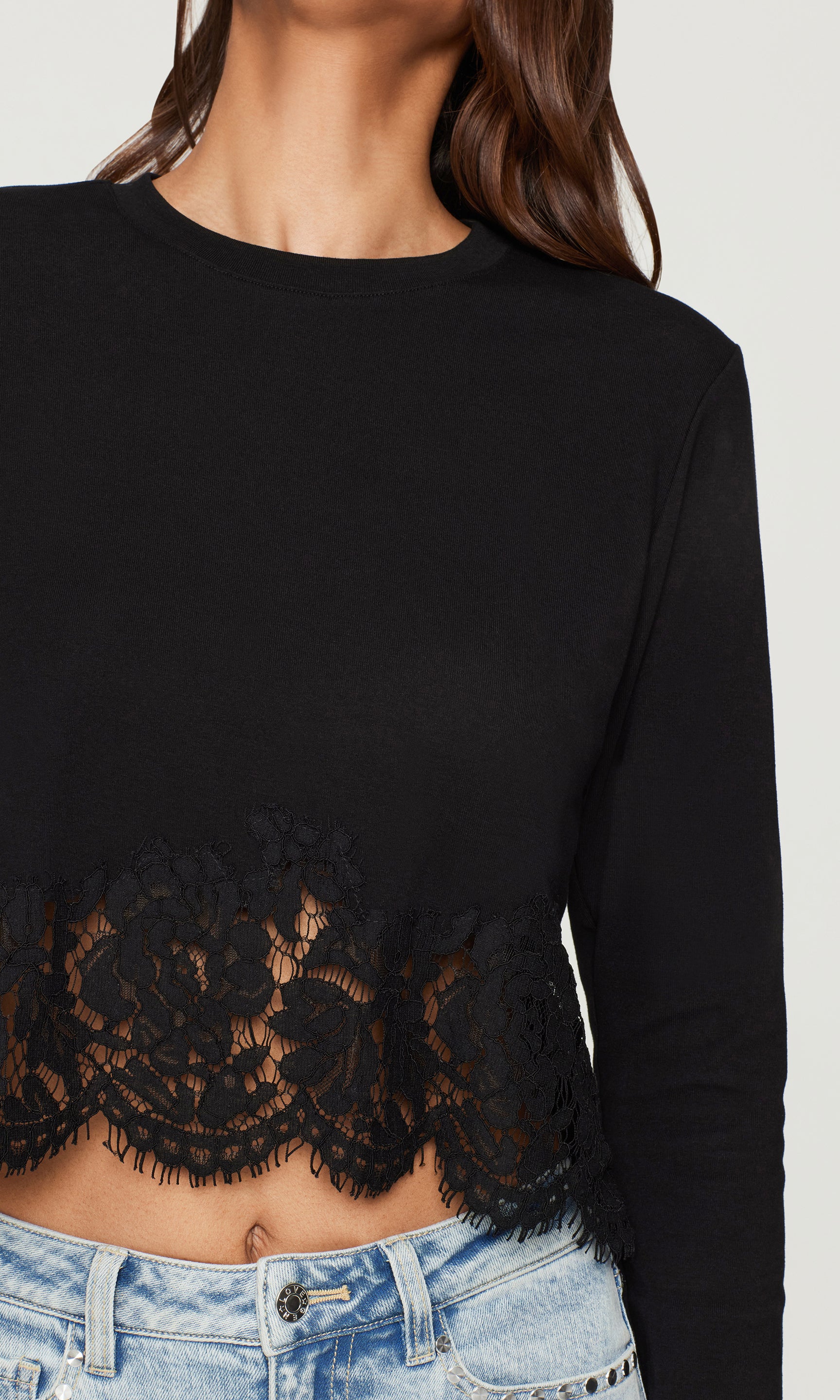 Black long-sleeve top with lace hem detail worn by a person on a white background