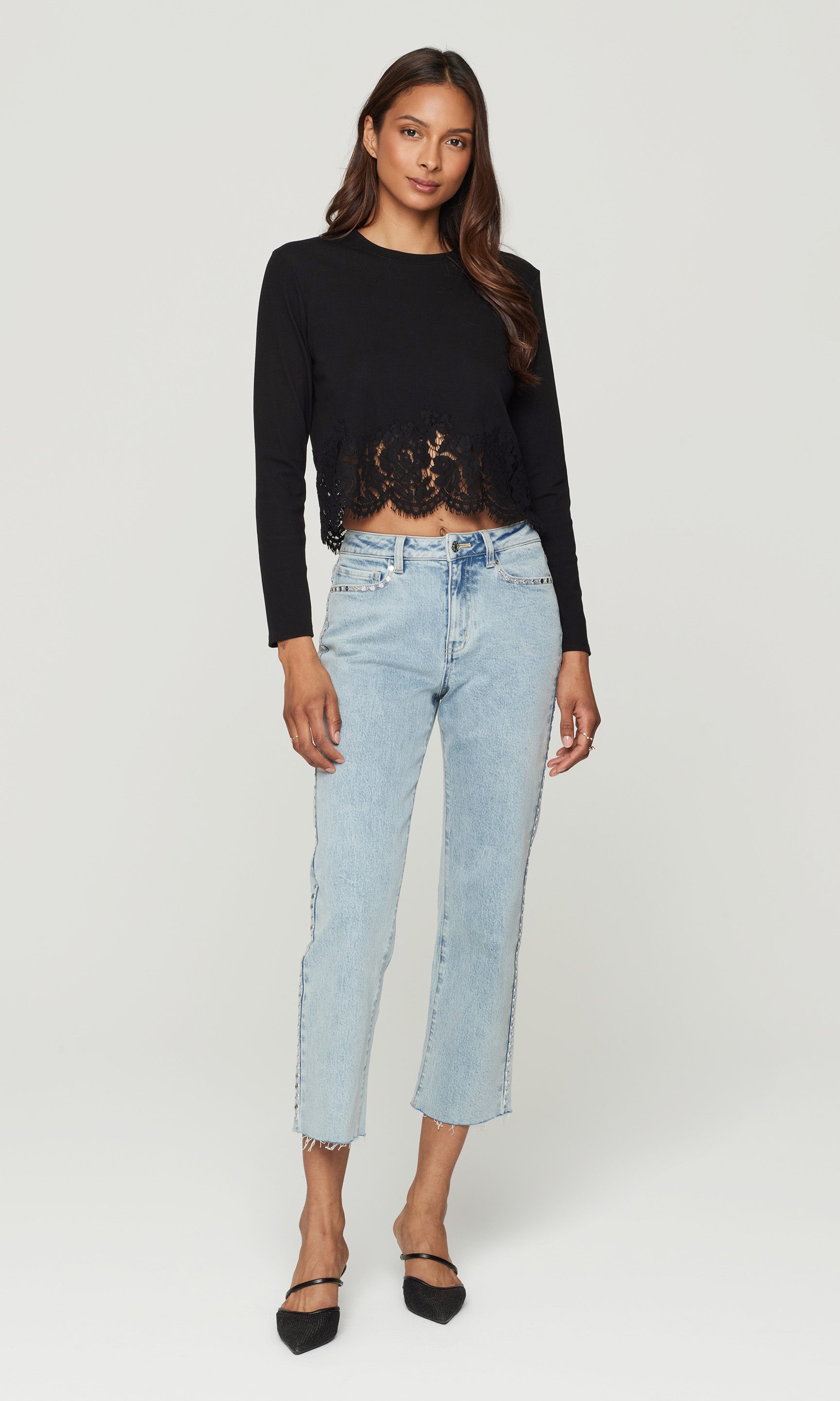 Woman wearing a black cropped sweater and light blue jeans on a white background