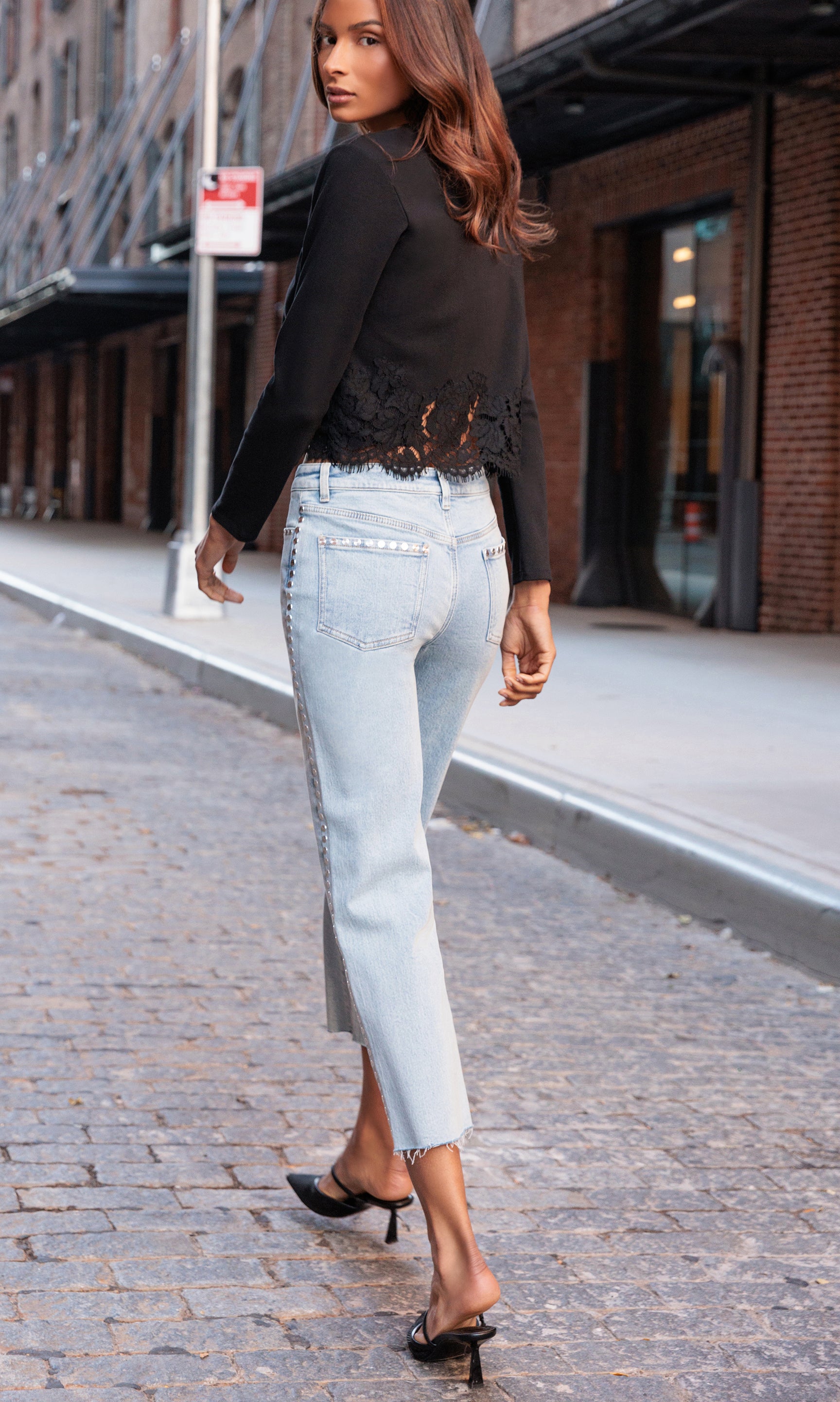 Back view of woman walking on a city street wearing a black top and light blue jeans.