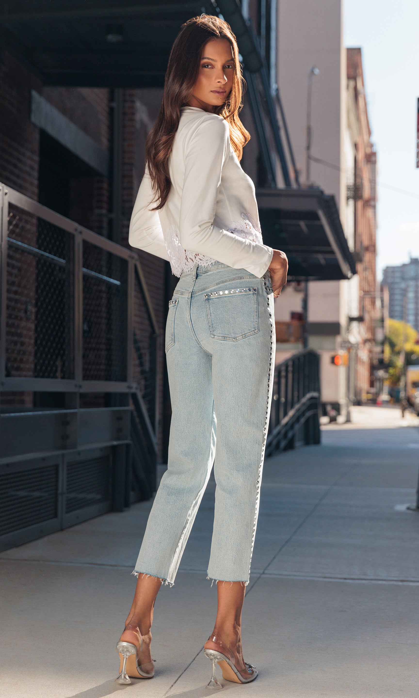 model standing on a sidewalk wearing a white top and light blue jeans