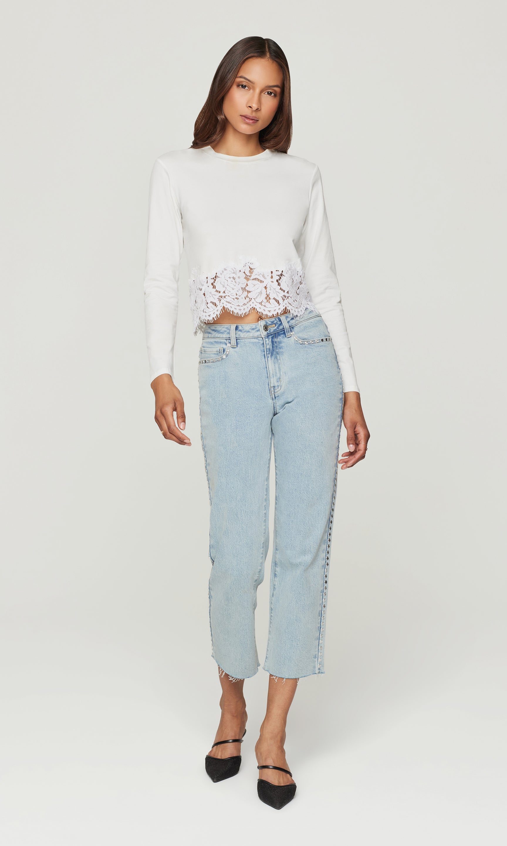 Woman wearing a white cropped top with lace details and light blue jeans on a white background