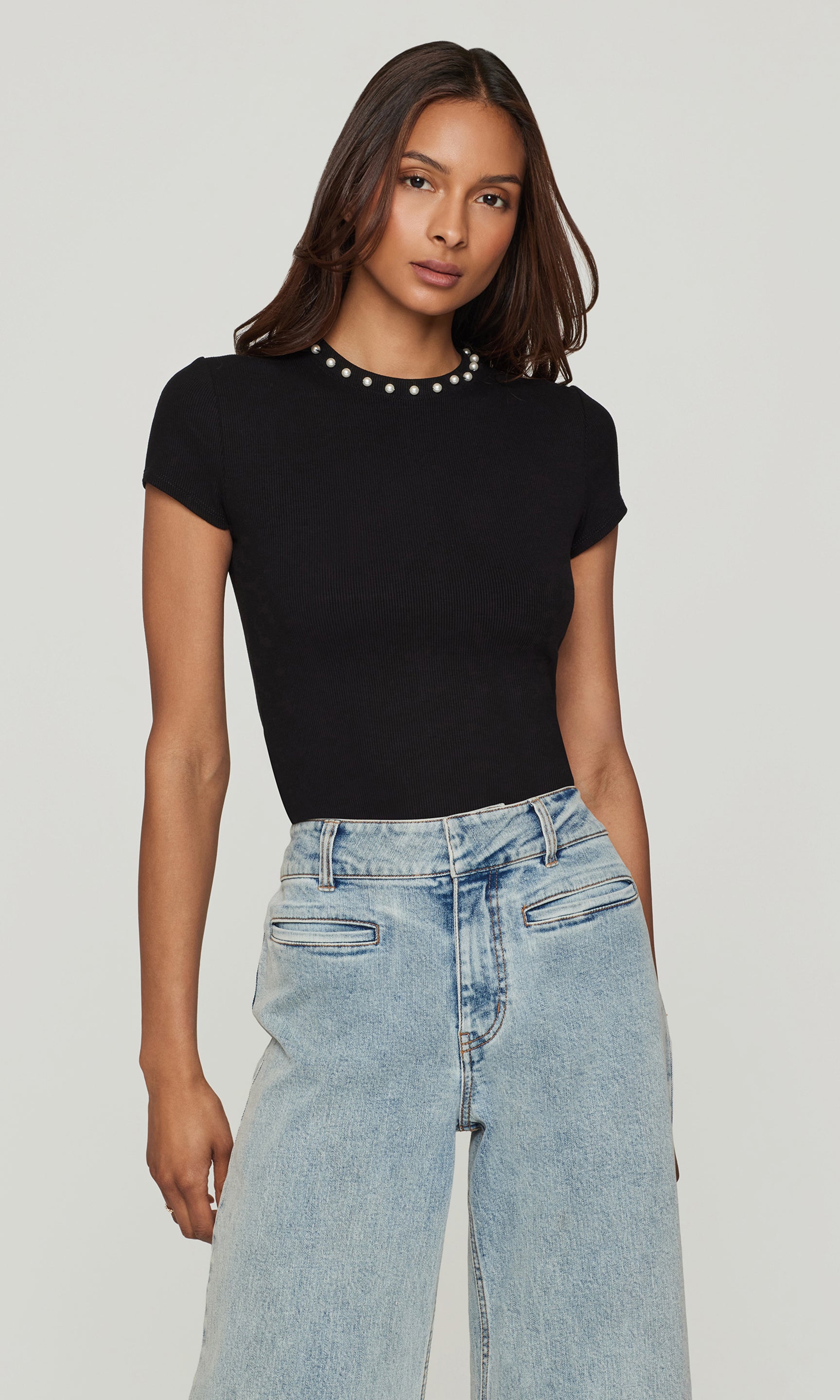 Woman wearing a black top and light blue jeans on a plain background