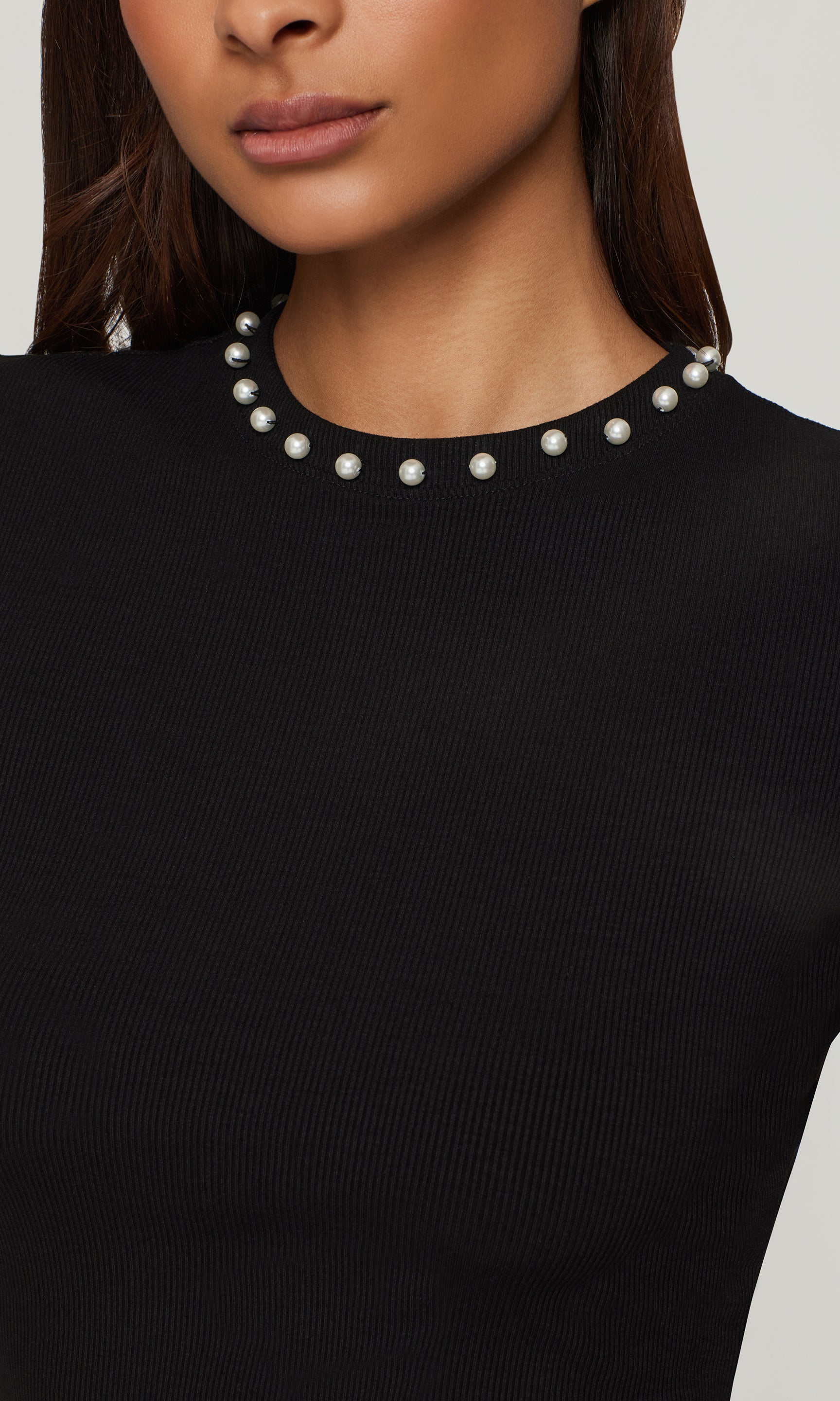 Close-up of black top with pearl collar worn by a model on a neutral background