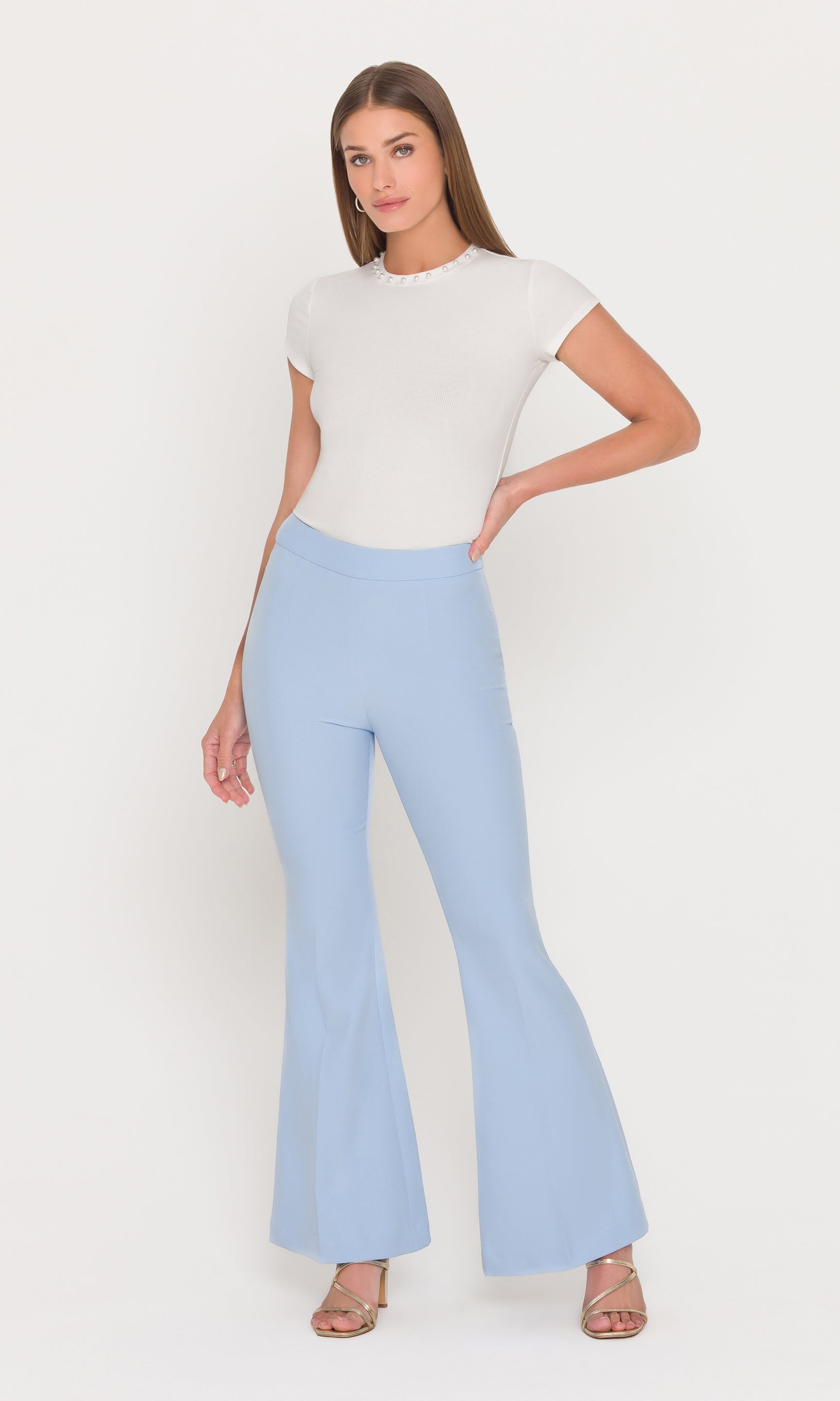 Full body image of woman wearing a white top and light blue flared pants on a white background