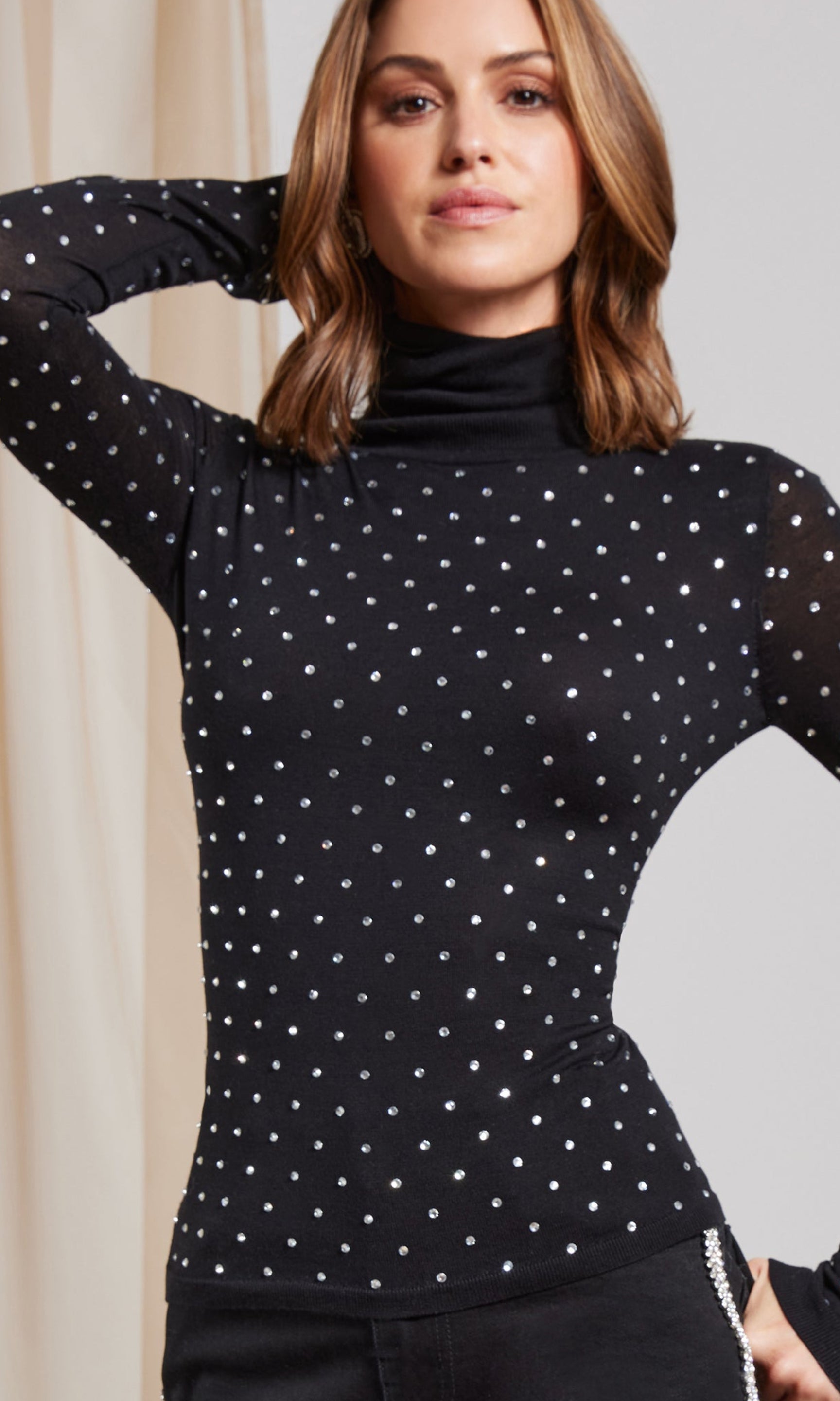 Woman wearing a black polka dot long-sleeve top against a neutral background