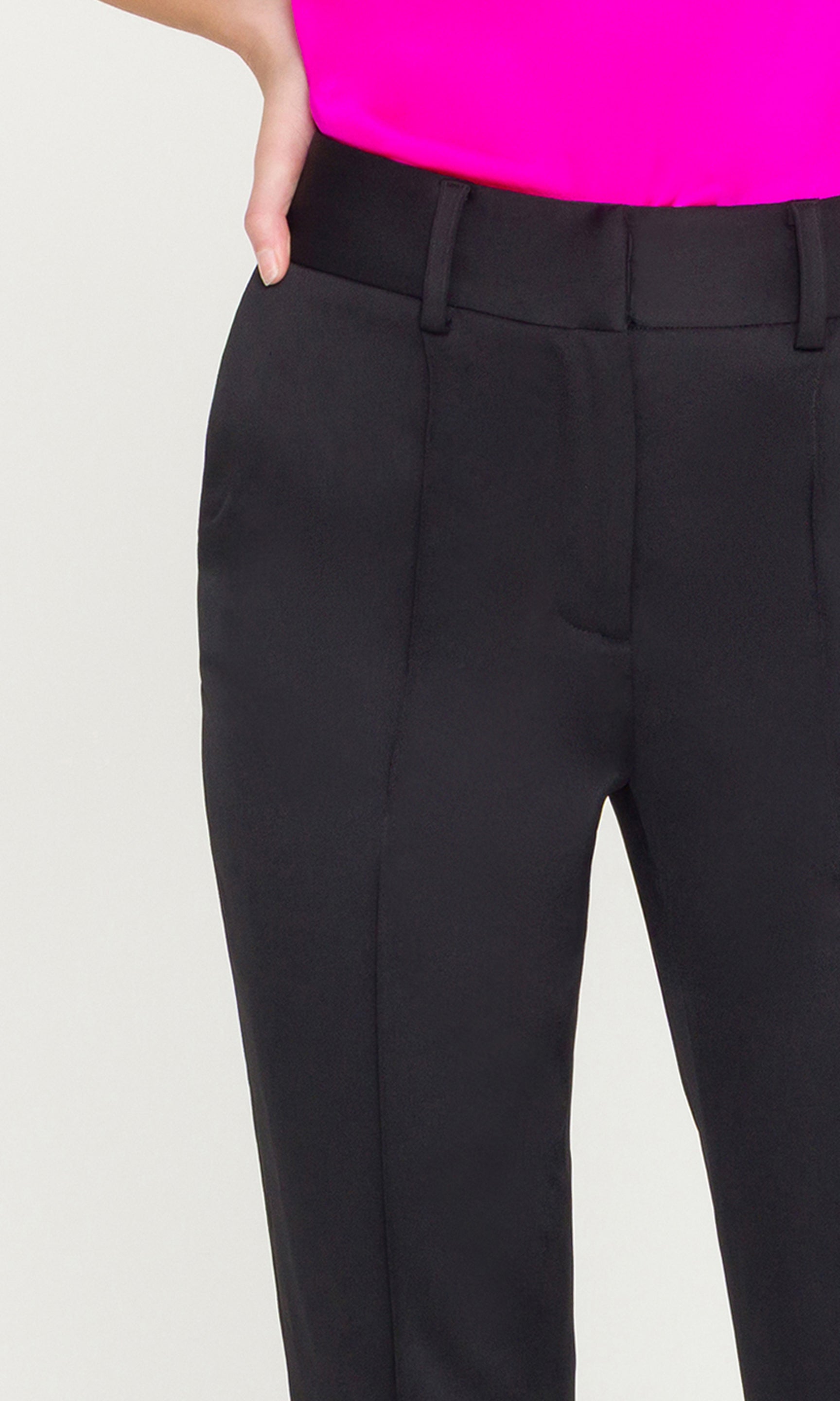 Black pants worn with a bright pink top on a light gray background