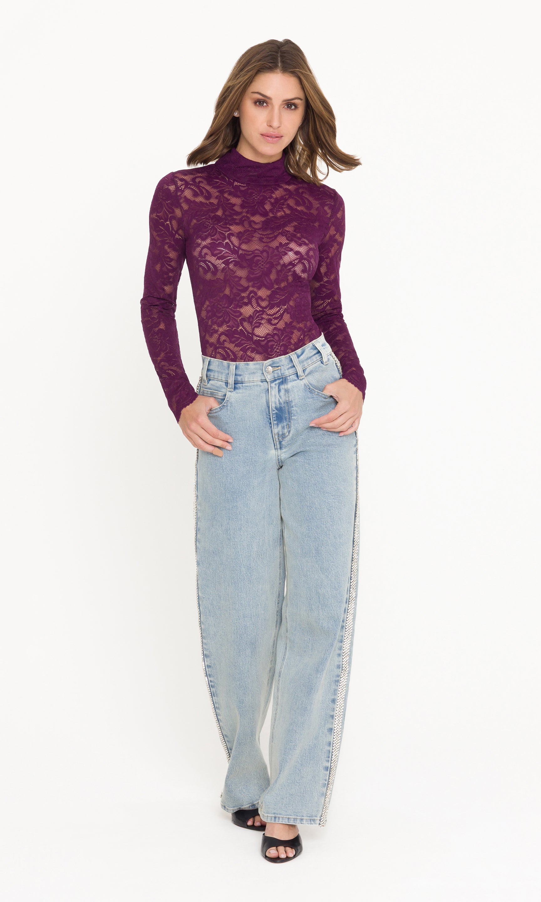 Full body image of model wearing a purple lace long-sleeve top and light blue jeans on a white background