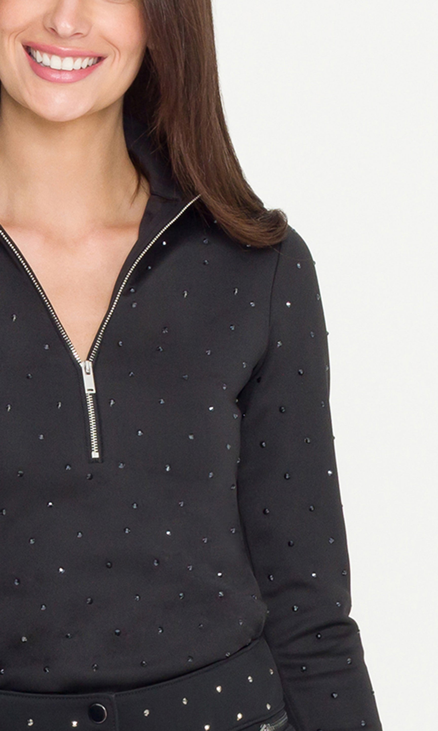 Woman wearing a black long-sleeve top with silver embellishments on a white background