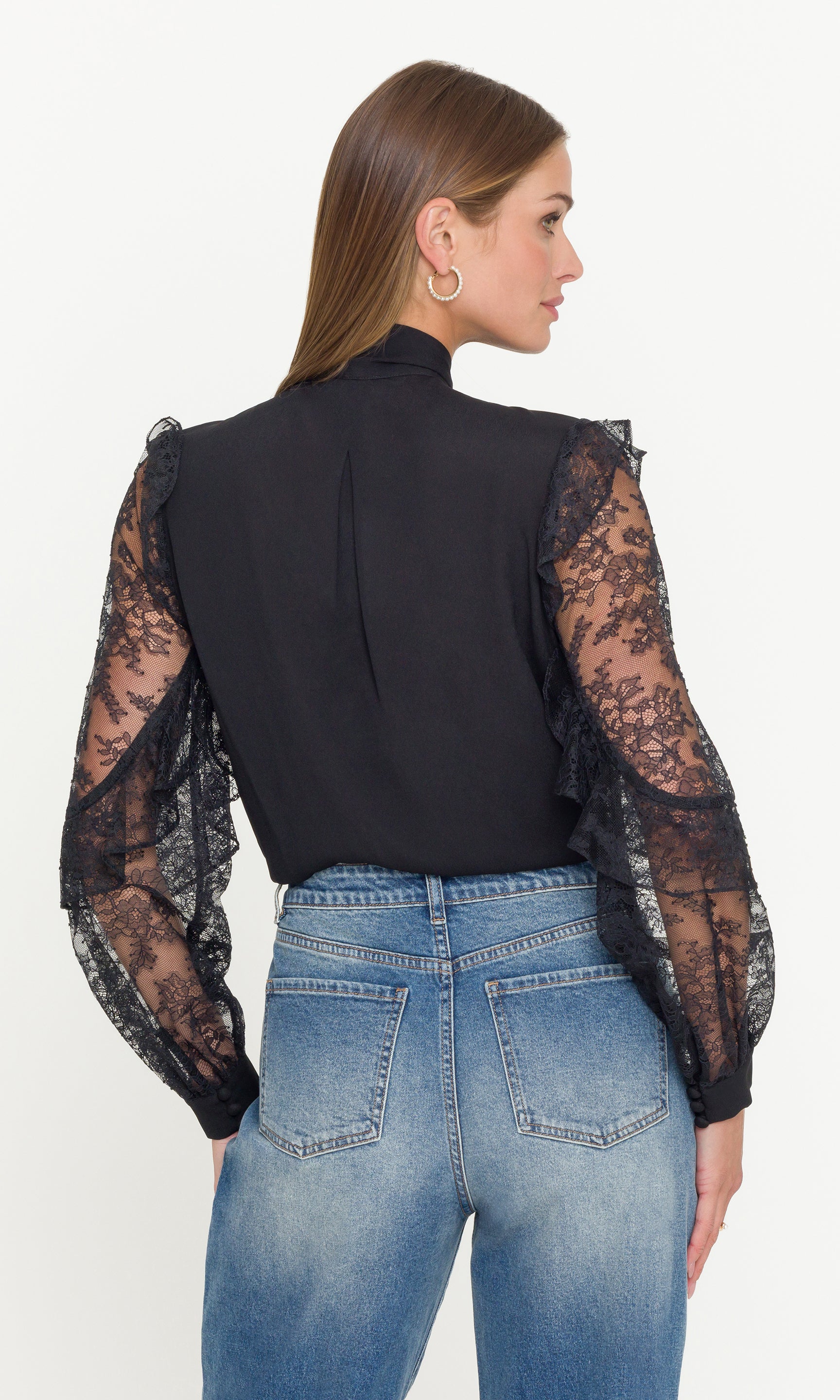 Woman wearing a black top with sheer lace sleeves and blue jeans on a white background