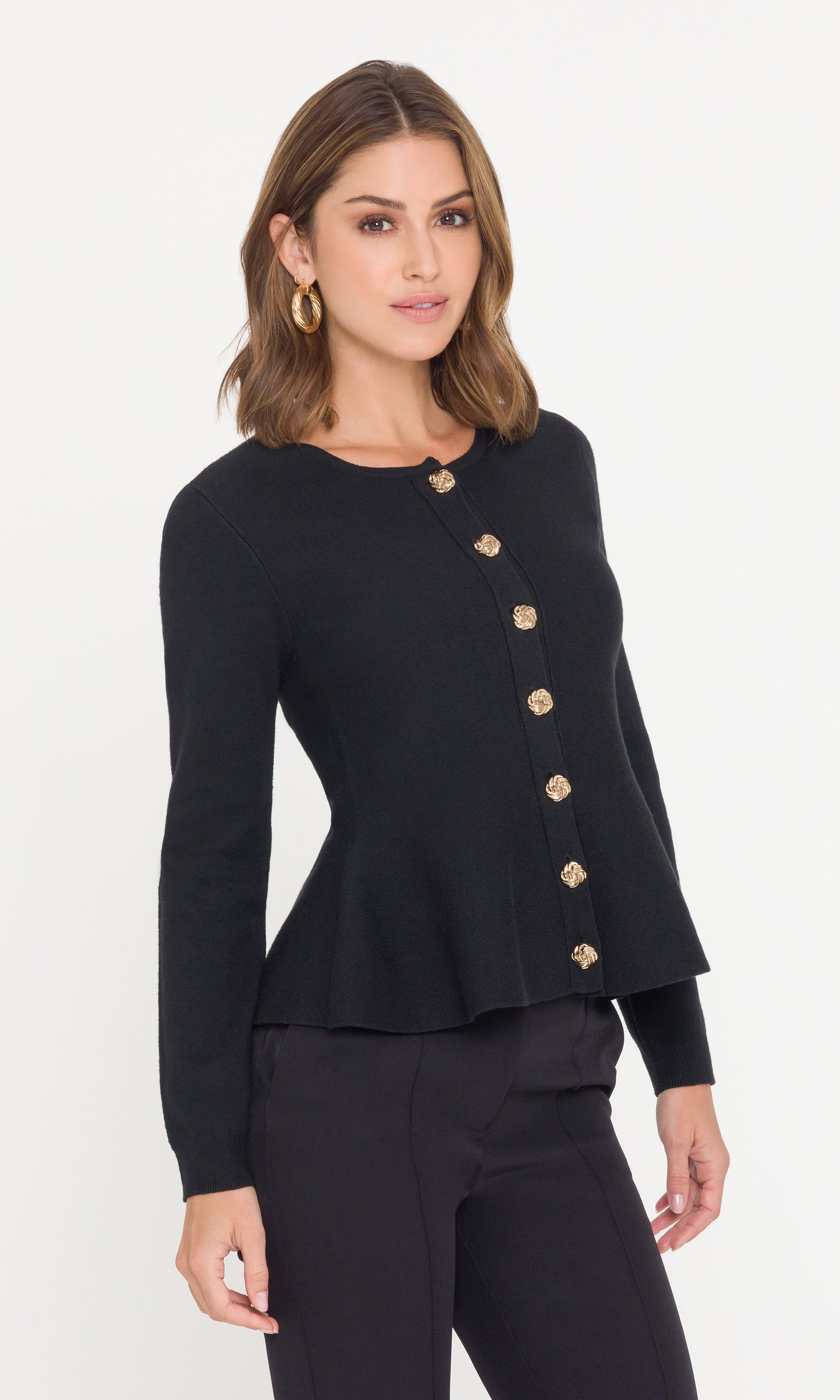 Side view of model wearing a black peplum sweater and black pants on a white background