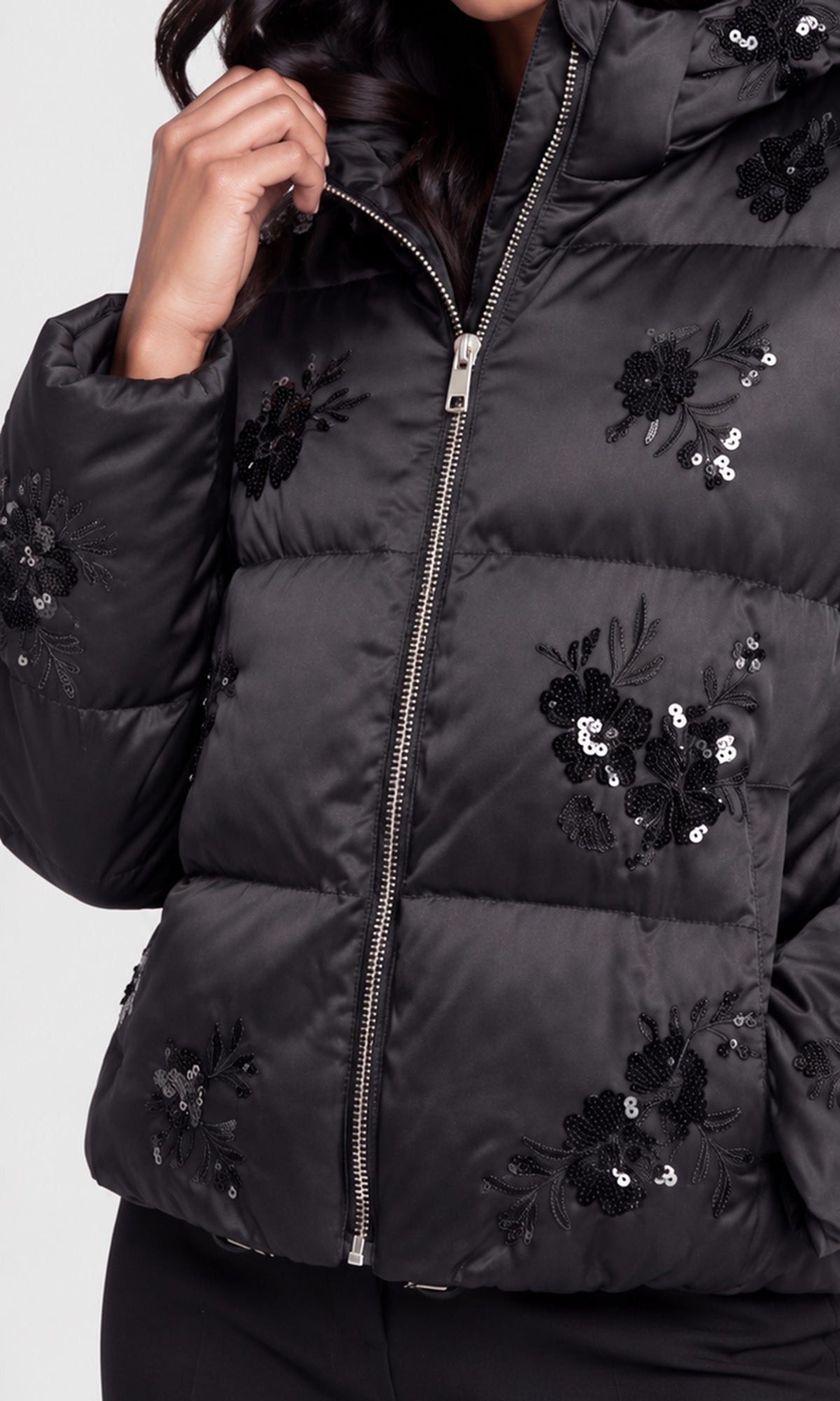 A close-up of a black puffer jacket with floral sequin and embroidered details, worn by a model.