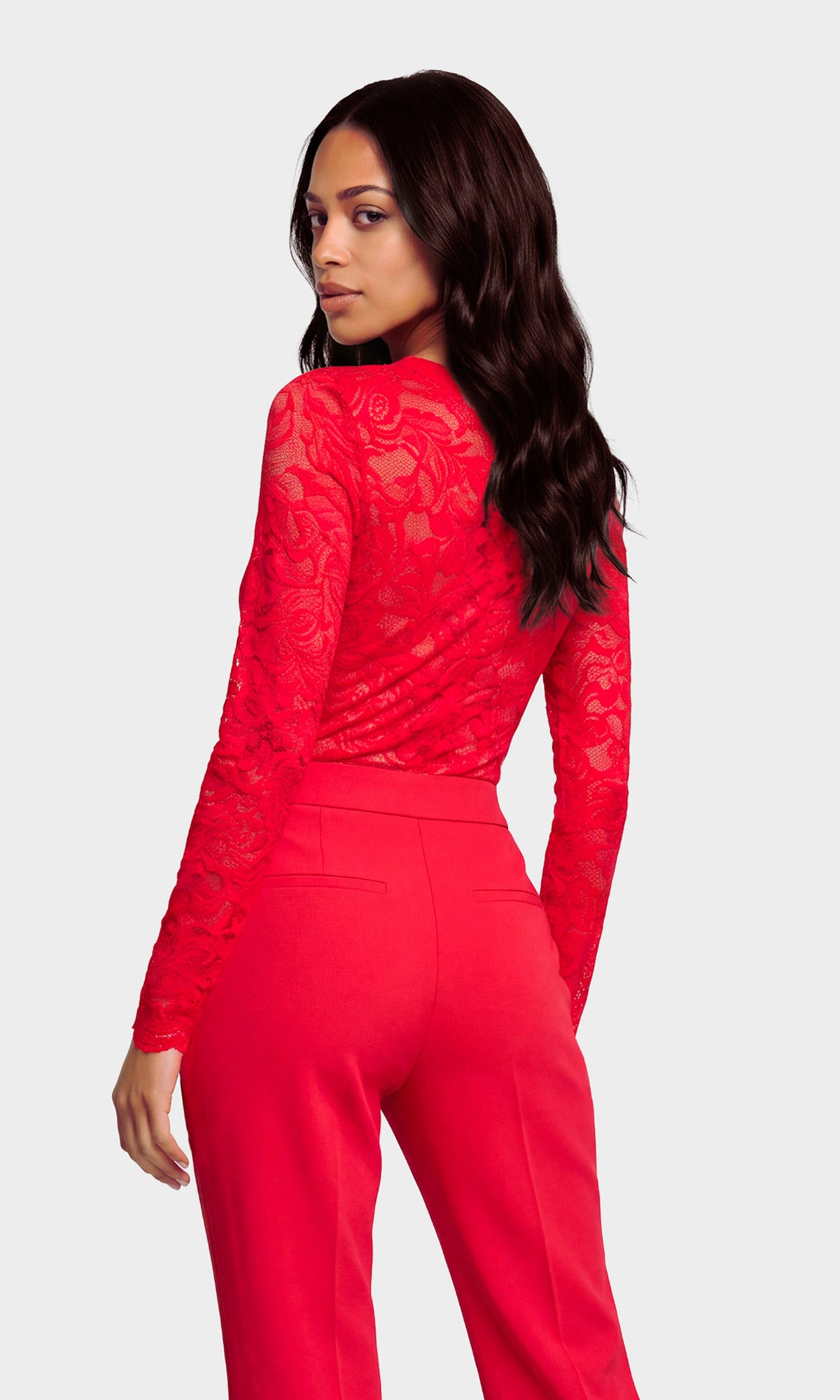Back view of model wearing a bright red long-sleeve lace top with a V-neckline, paired with matching red high-waisted pants.