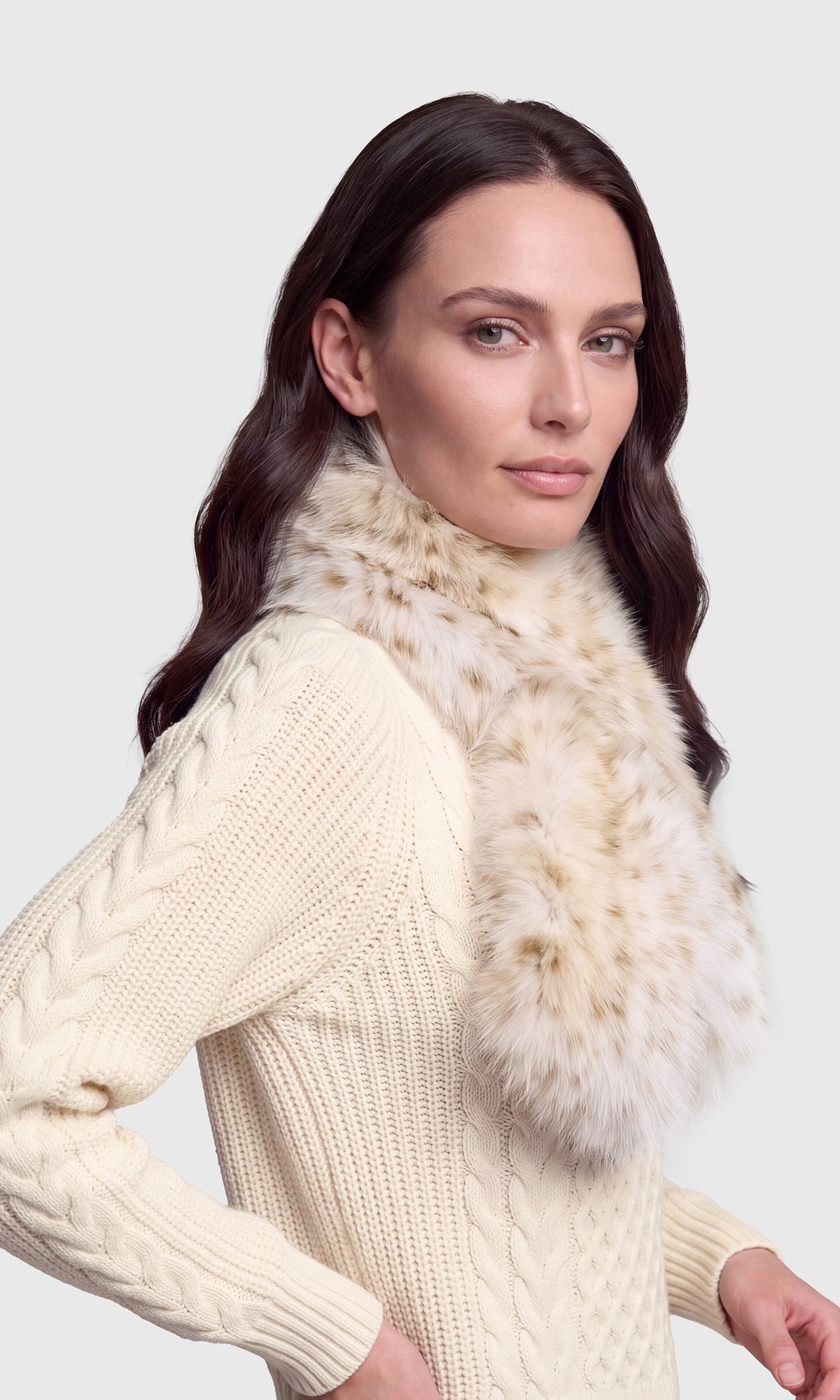 Side view of model wearing a cream cable-knit sweater and a fluffy beige and white faux fur collar.