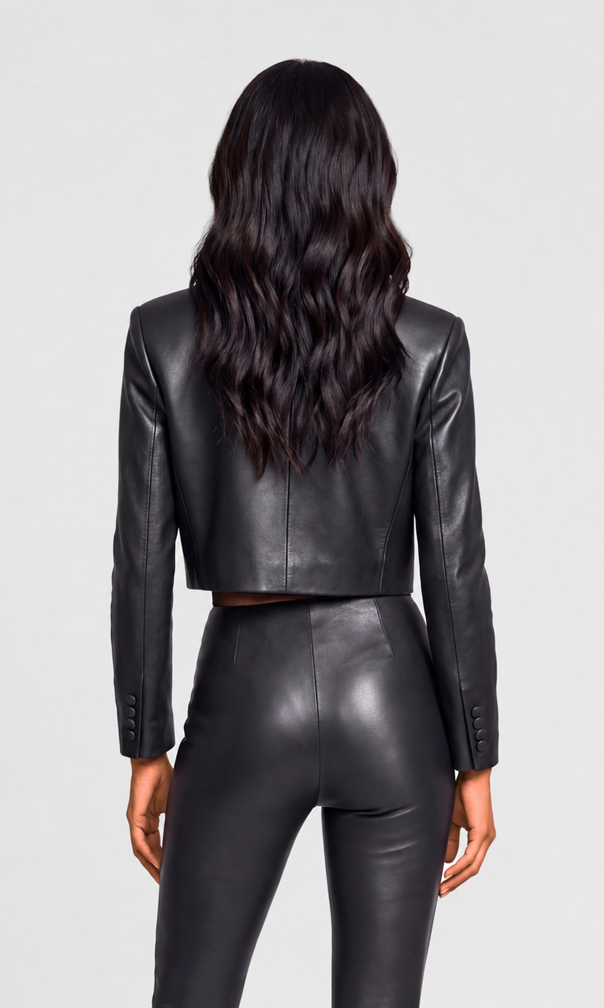 Back view of model wearing a black cropped faux-leather jacket and matching black faux-leather leggings.
