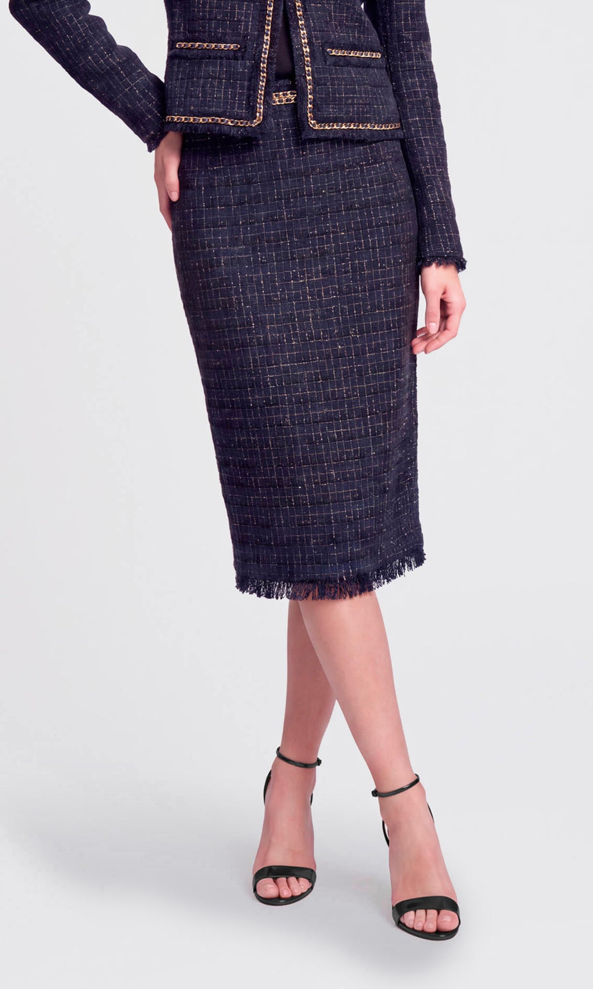 Model wearing a navy blue tweed midi-length skirt suit with gold trim, featuring a matching jacket.