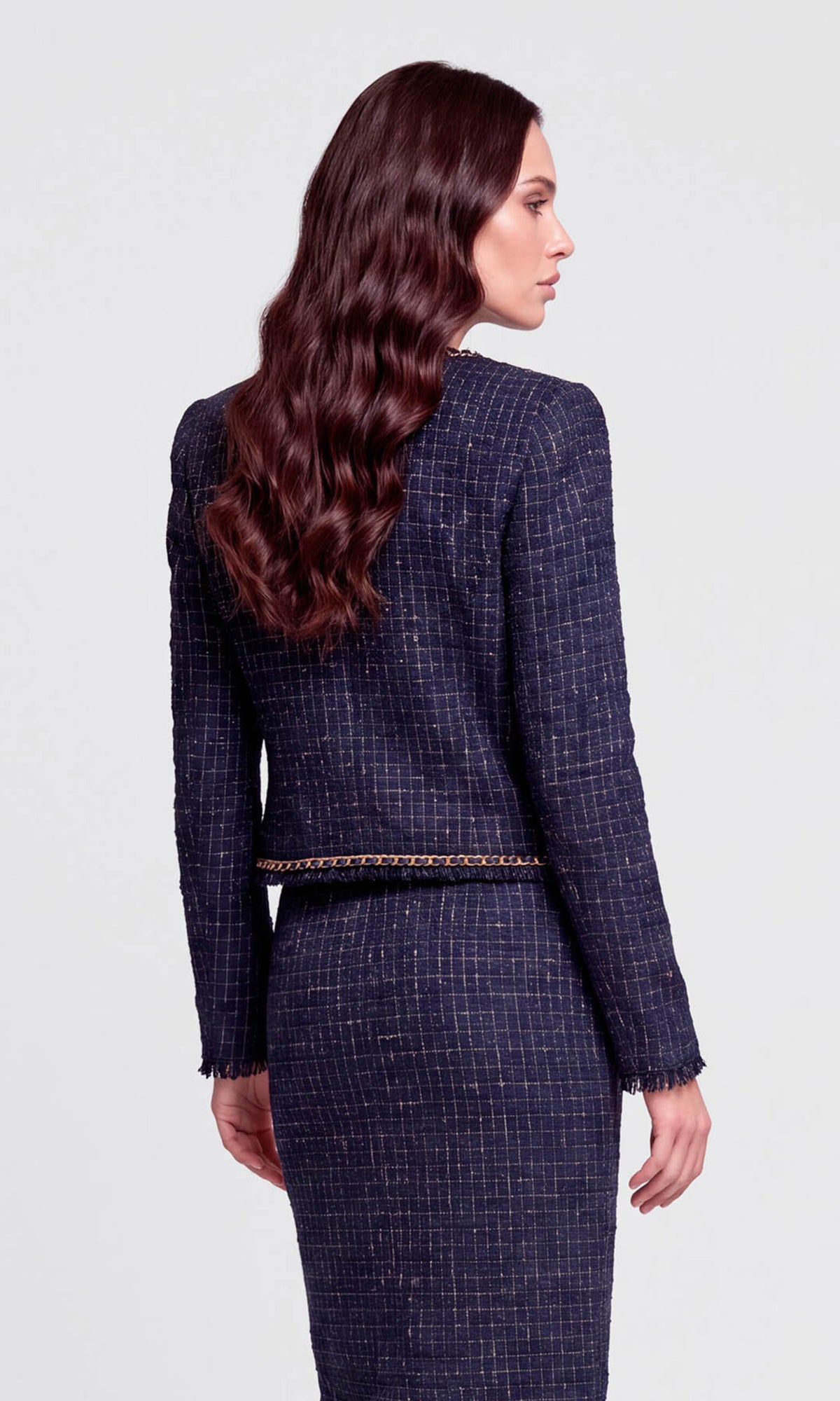 Back view of model wearing a navy tweed jacket with gold accents and a matching skirt.