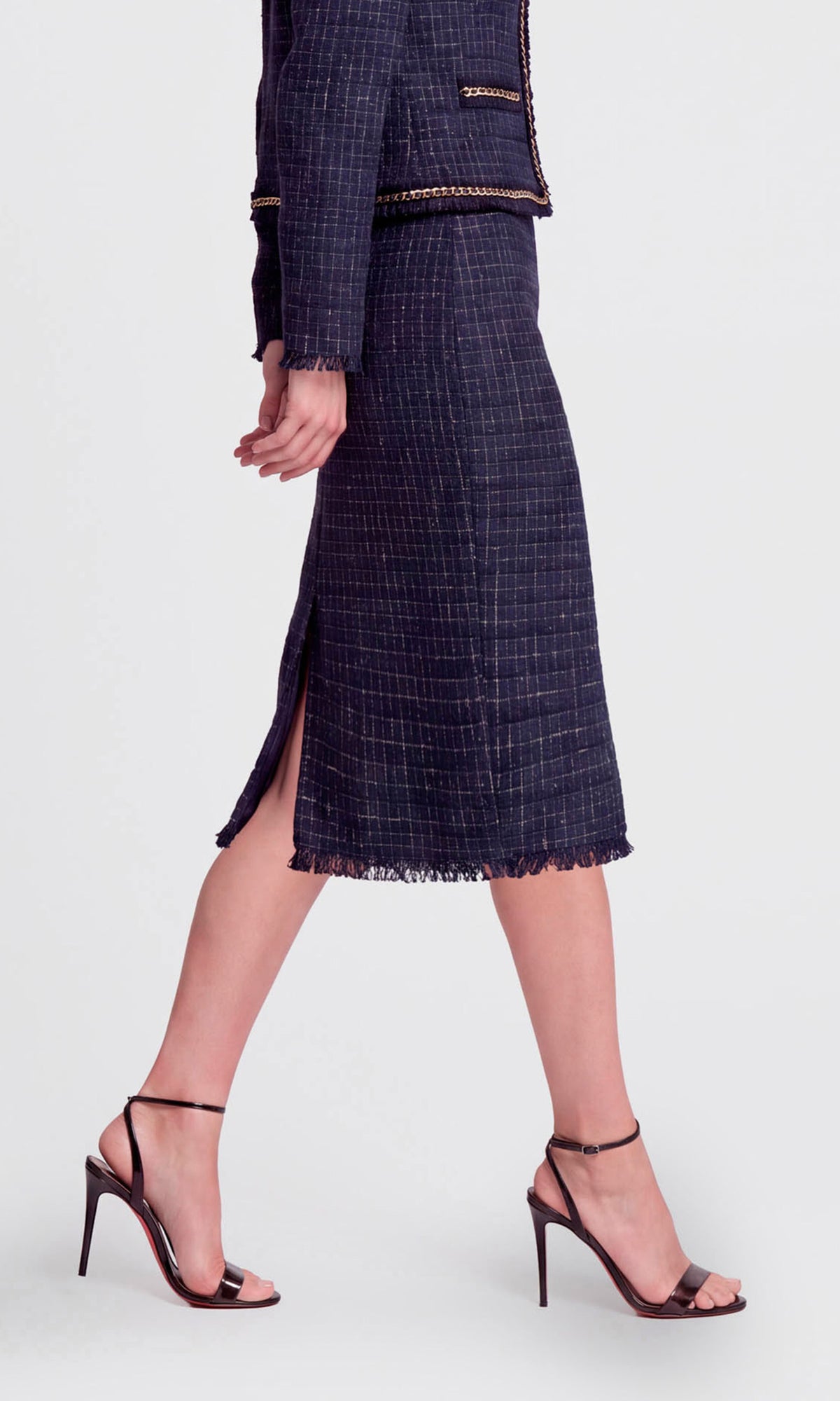 Side view of model wearing a navy blue tweed midi-length skirt suit with gold trim, featuring a matching jacket.