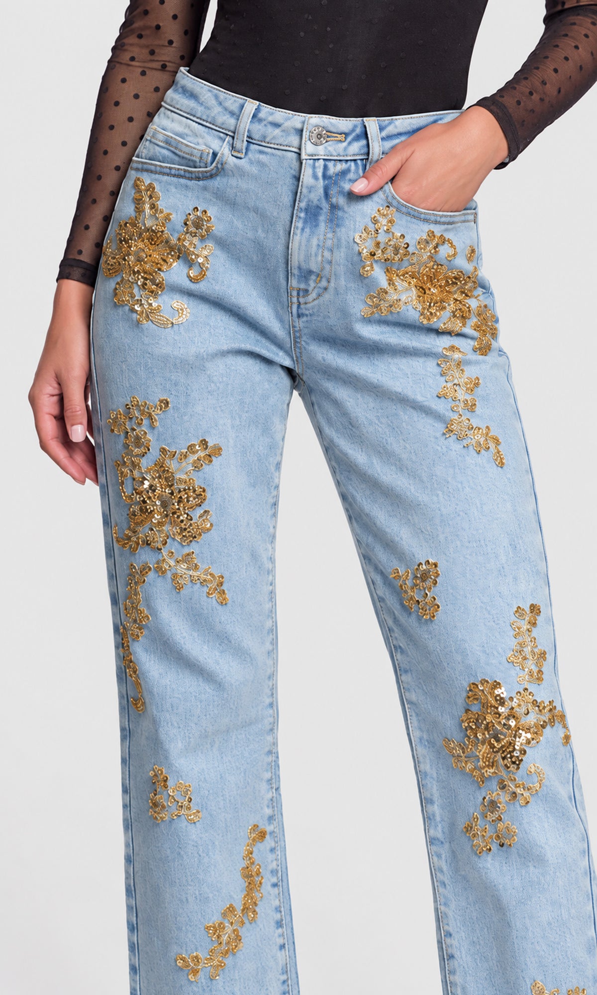 Close-up of light wash blue jeans with gold sequined floral embroidery on the thighs.