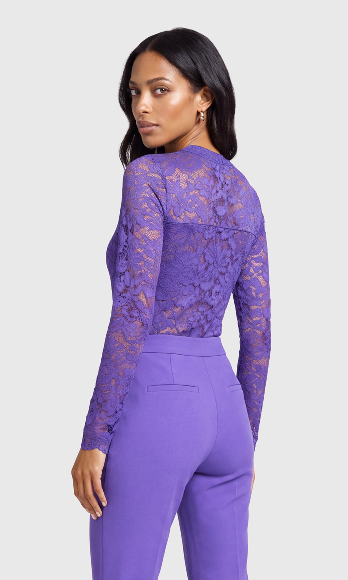 A woman shown from the back wearing a purple long-sleeve lace top and matching purple trousers.