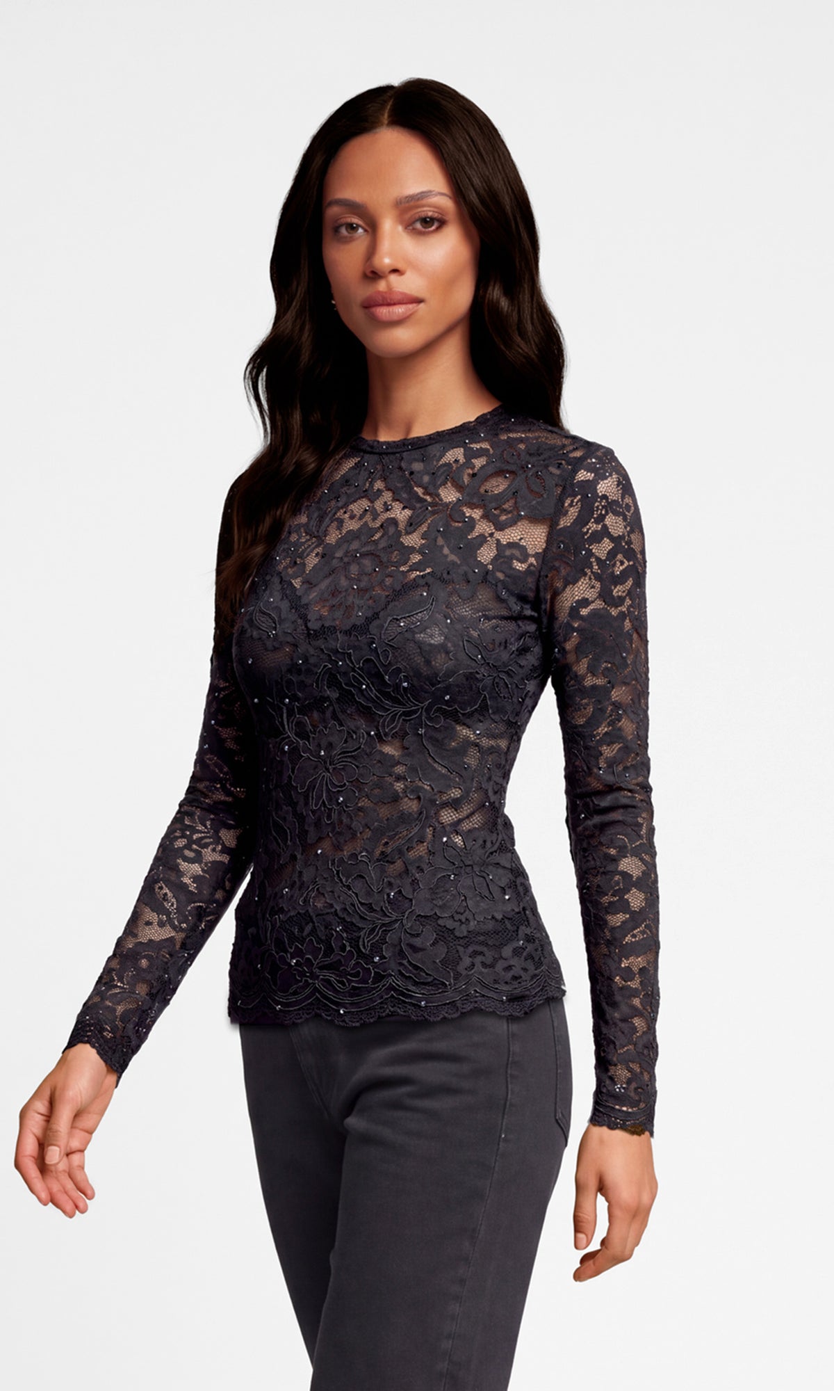 Side view of model wearing a dark charcoal gray lace long-sleeve top with a crew neck, paired with dark gray pants.