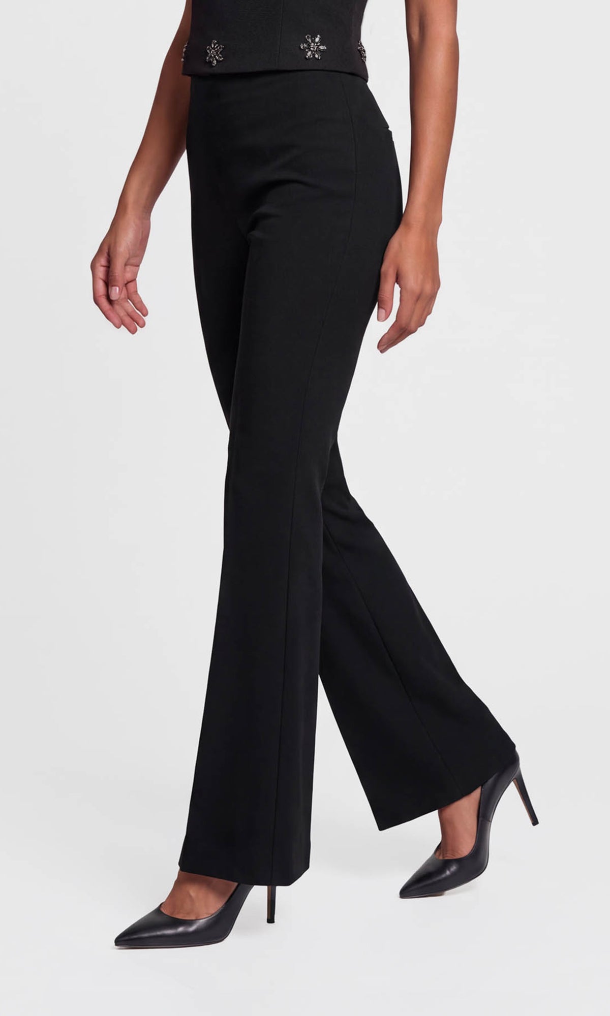 Side view of model wearing black high-waisted flared pants with a straight waistband, paired with black pointed-toe heels.