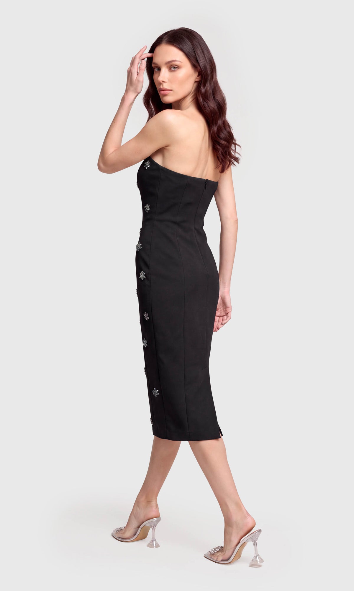 Model wearing a strapless black midi dress with decorative silver embellishments down the front.
