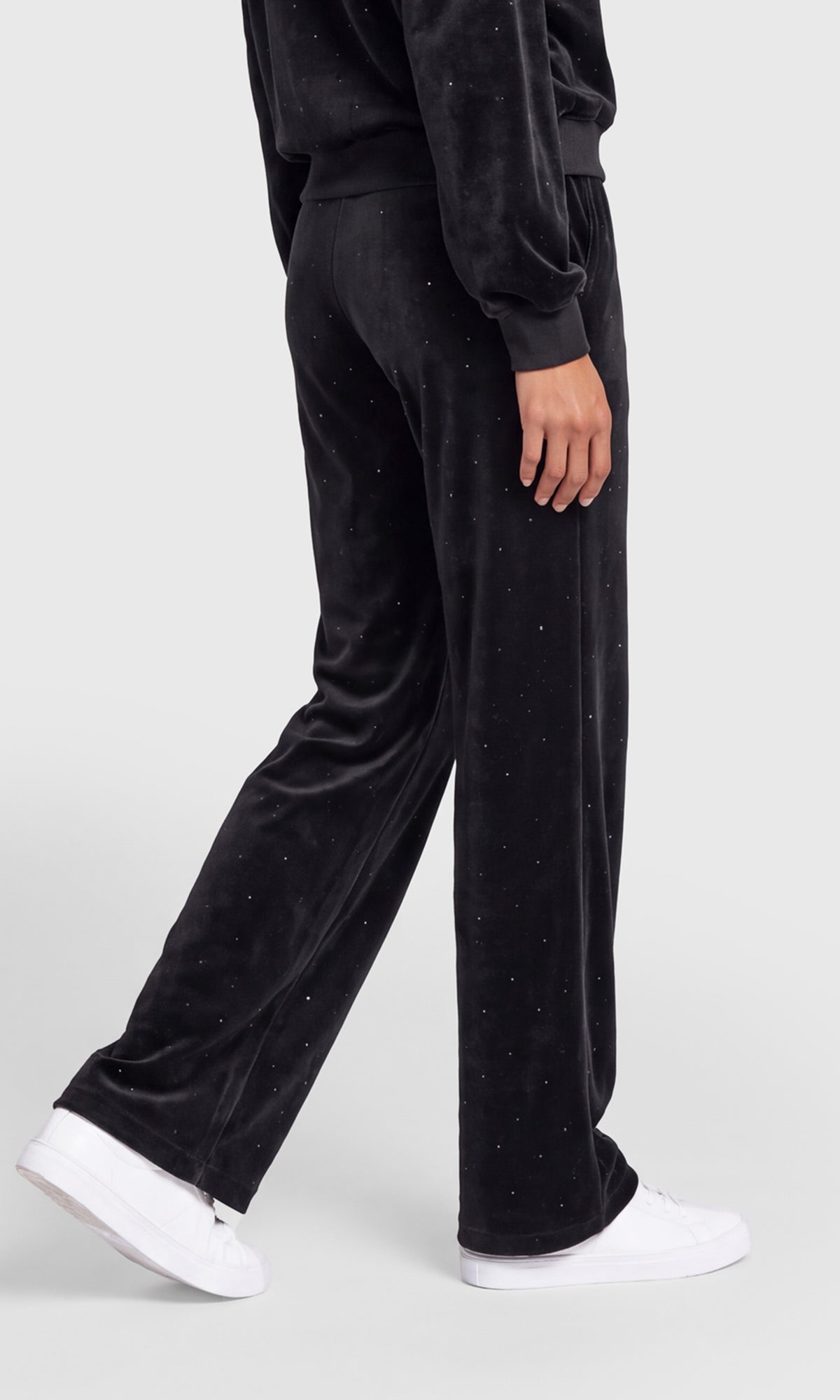 Side view of black velvet wide-leg pants with small silver rhinestone embellishments, shown on a model wearing white sneakers.