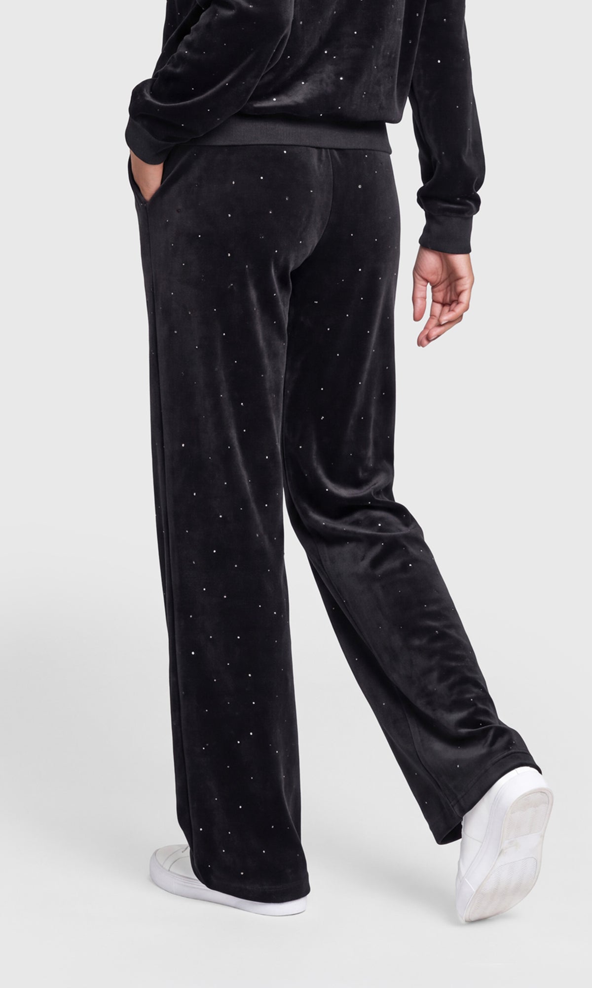 Back view of black velvet wide-leg pants with small silver rhinestone embellishments, shown on a model wearing white sneakers.