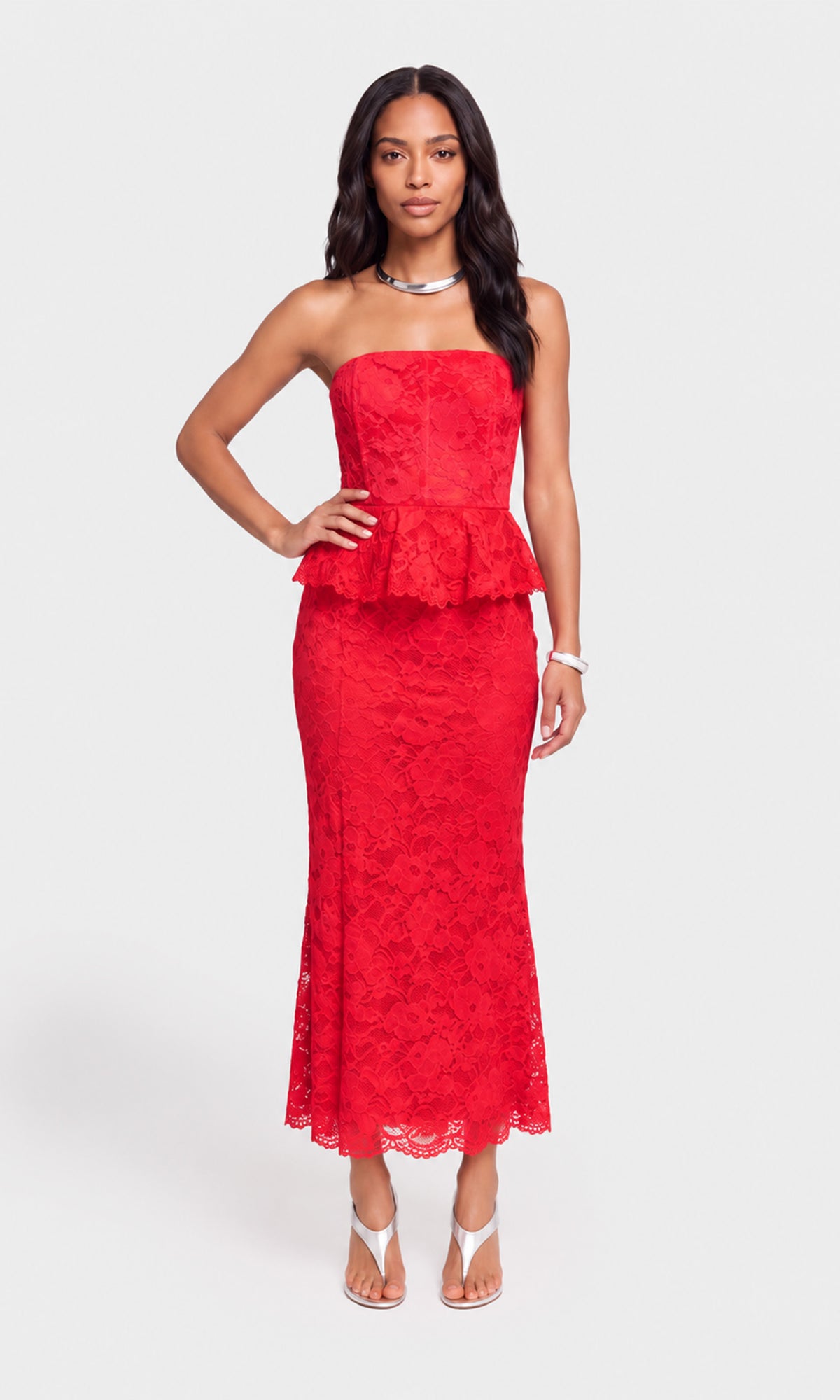 A woman modeling a bright red strapless lace maxi dress with a peplum waist, paired with white heeled sandals.
