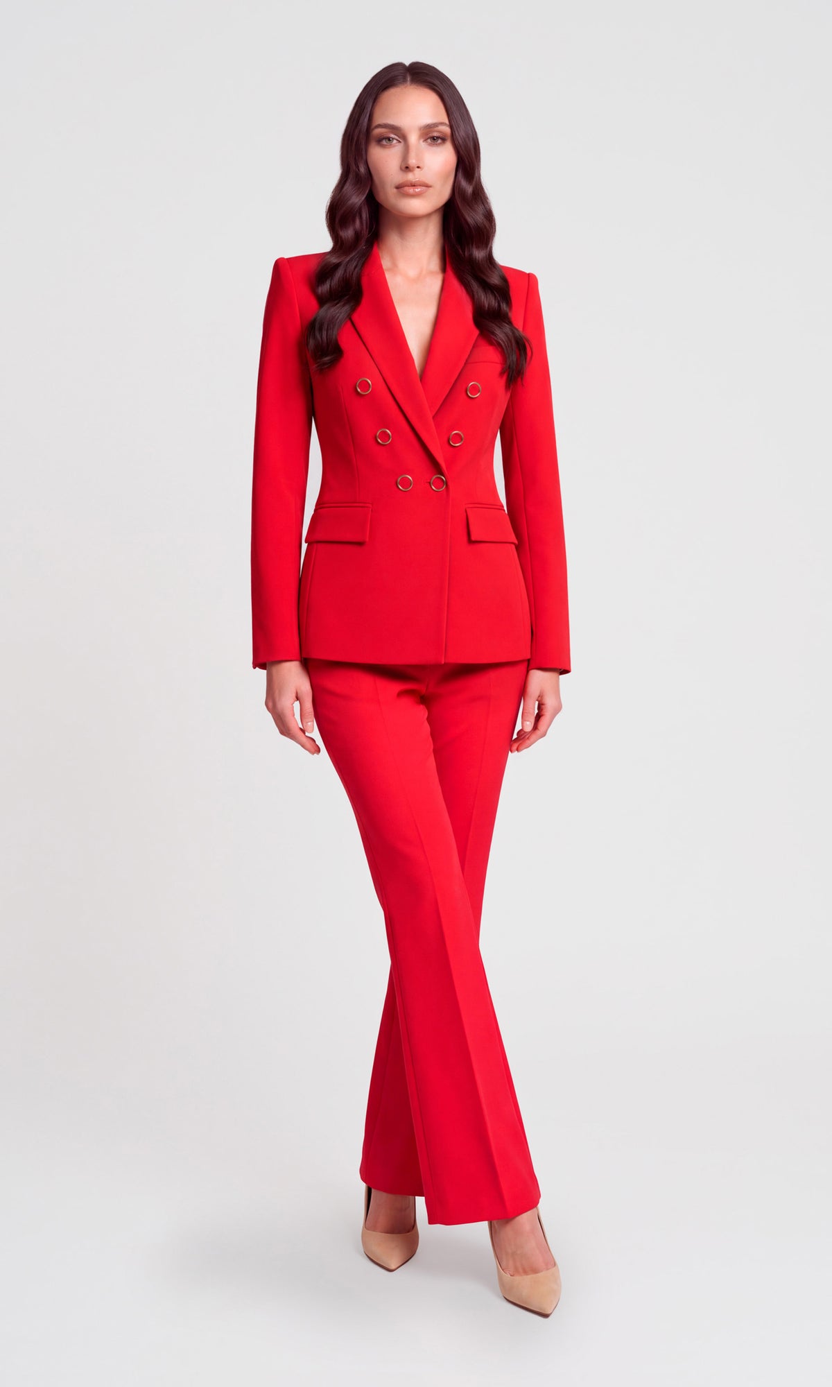 A woman modeling a bright red double-breasted blazer and matching flared pants suit, paired with nude heels.