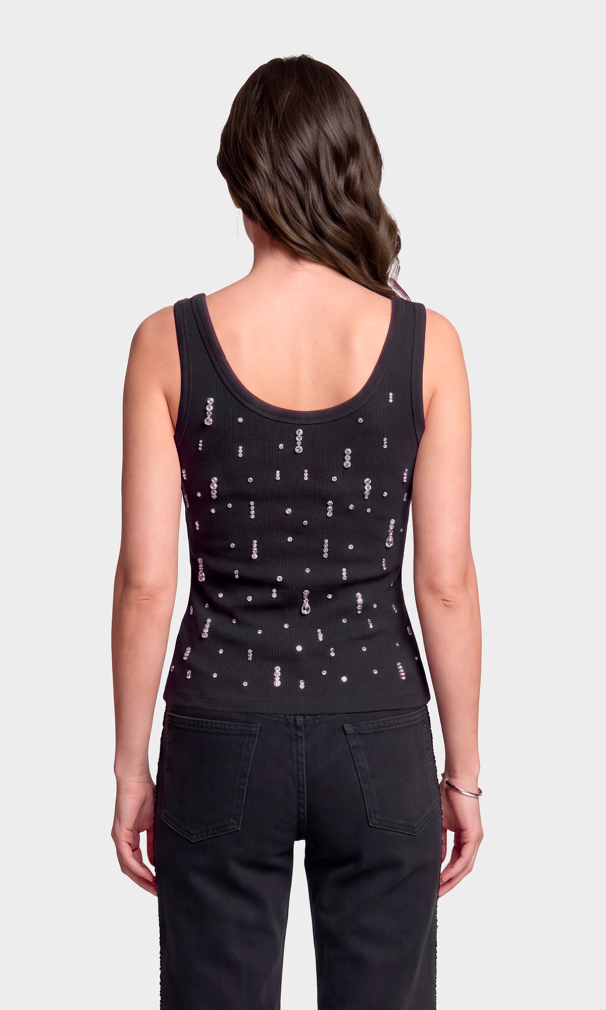 Back view of model wearing a black racerback tank top with a scattered white and silver graphic print, paired with black jeans.