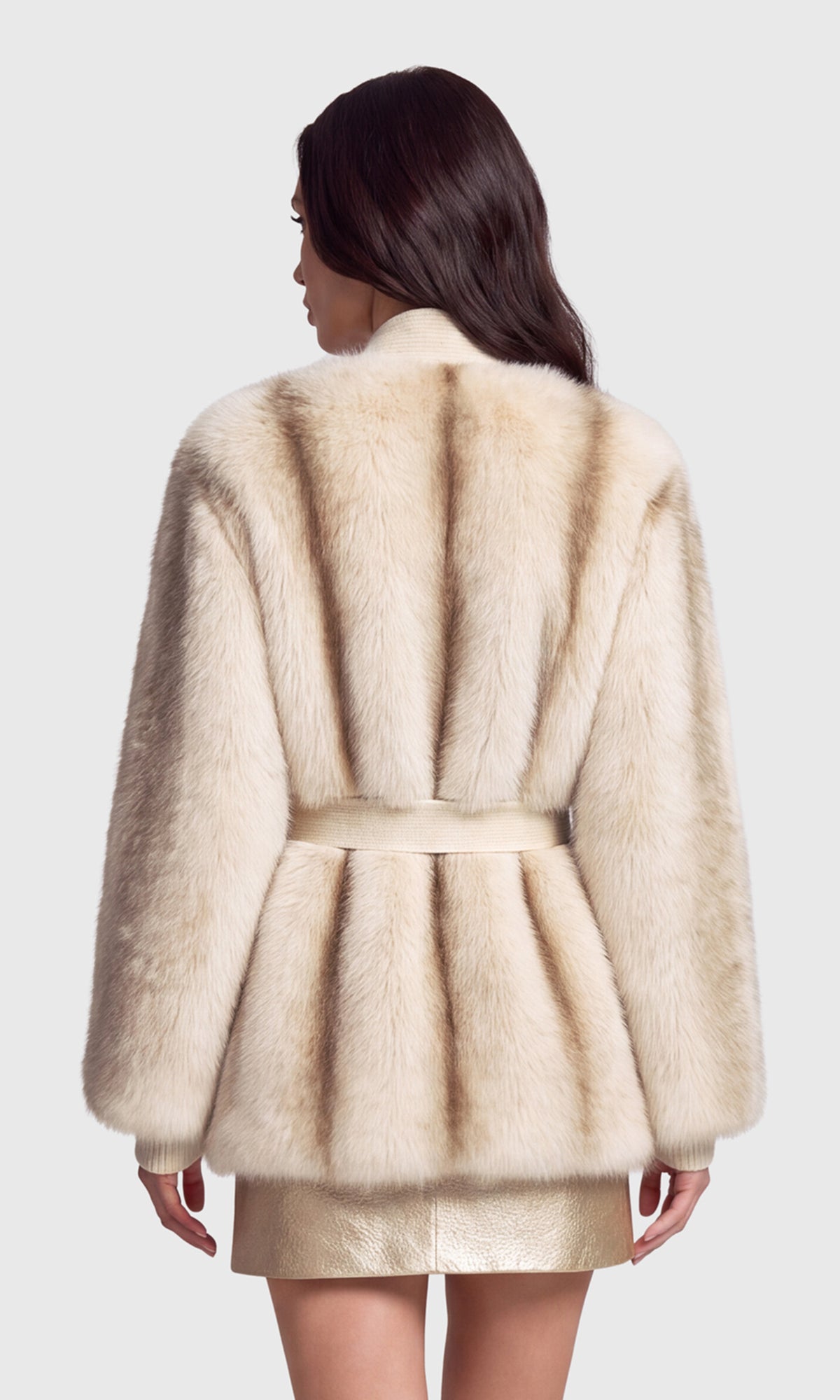 Back view of model wearing a cream-colored fur jacket with a matching belt, paired with a metallic gold skirt.