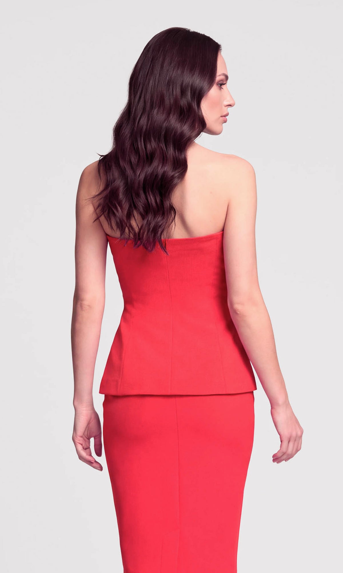 Back view of model wearing a red strapless peplum top with a matching skirt.