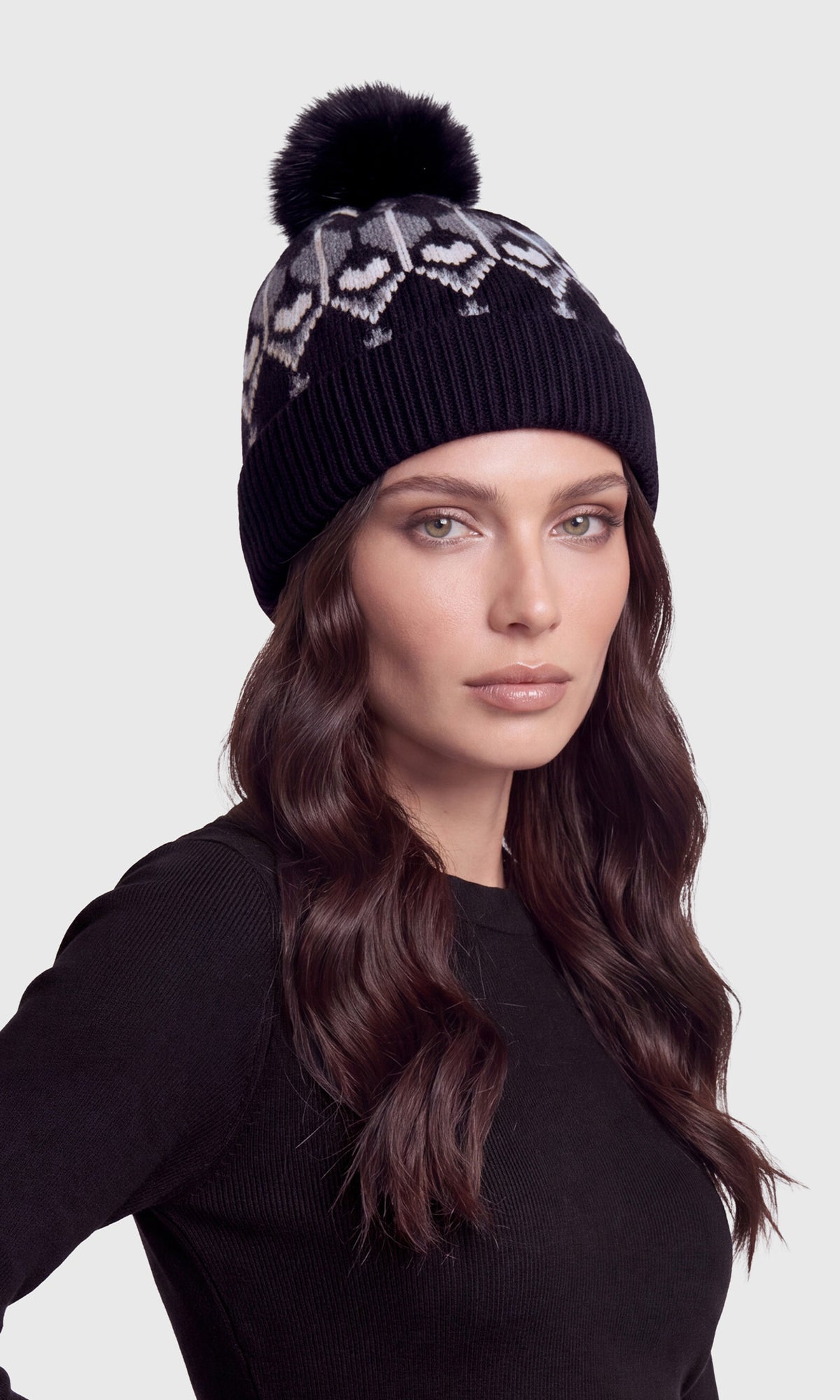 A woman wearing a black knit beanie with a pom-pom and a gray geometric pattern on the upper portion.