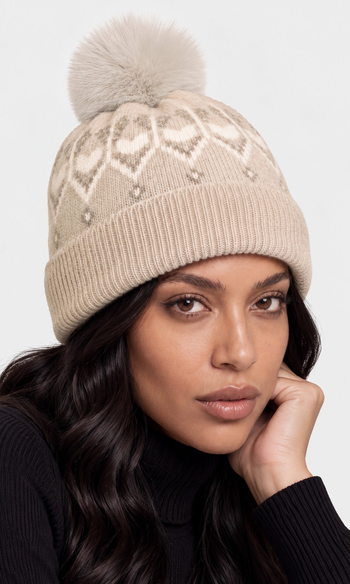 A woman wearing a beige knit pom-pom beanie with a cream geometric pattern.