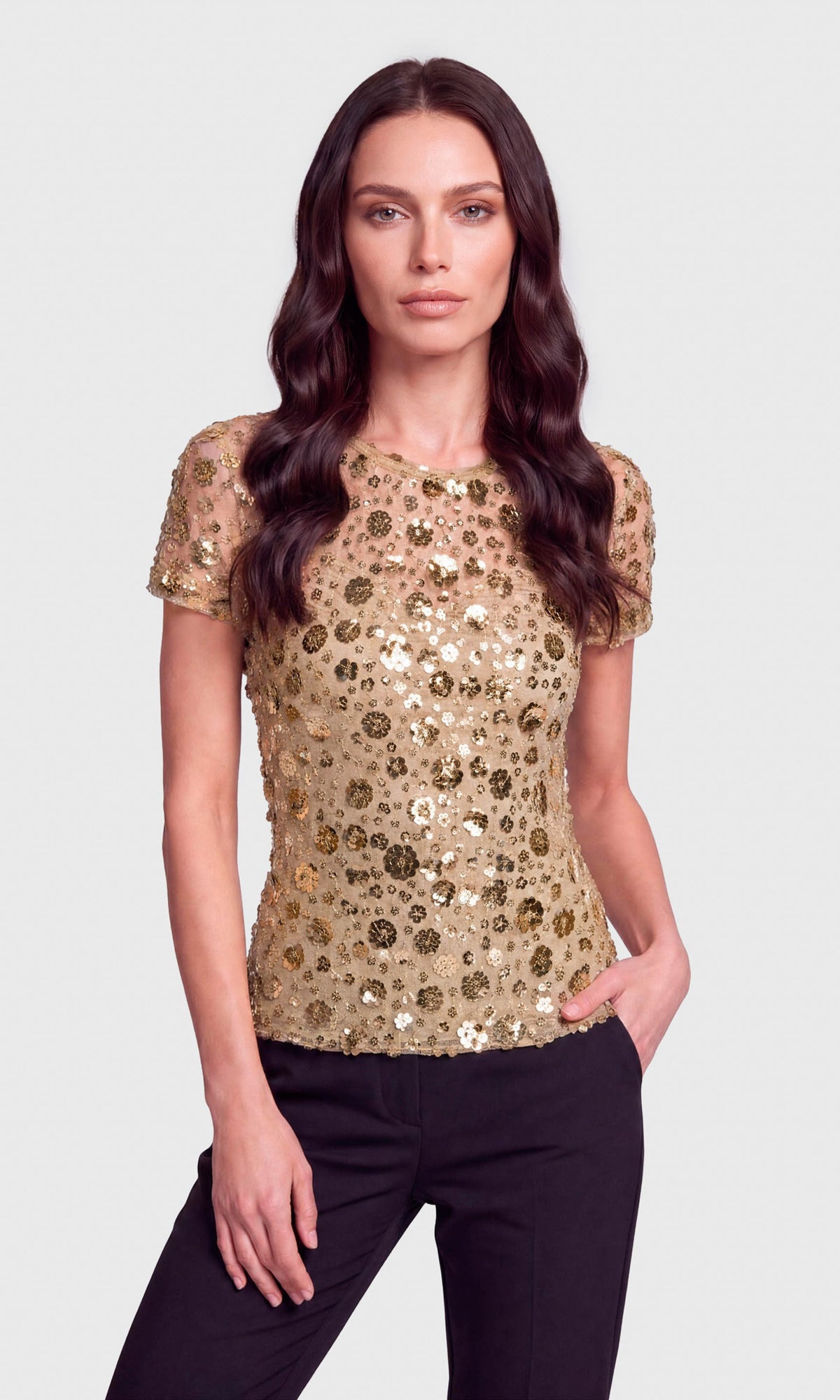 A woman modeling a short-sleeve gold sequined top with black pants.