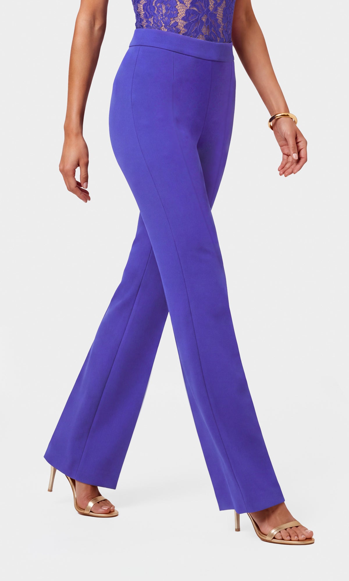 A model wearing high-waisted, wide-leg purple trousers with a sheer lace bodice top and gold heeled sandals.