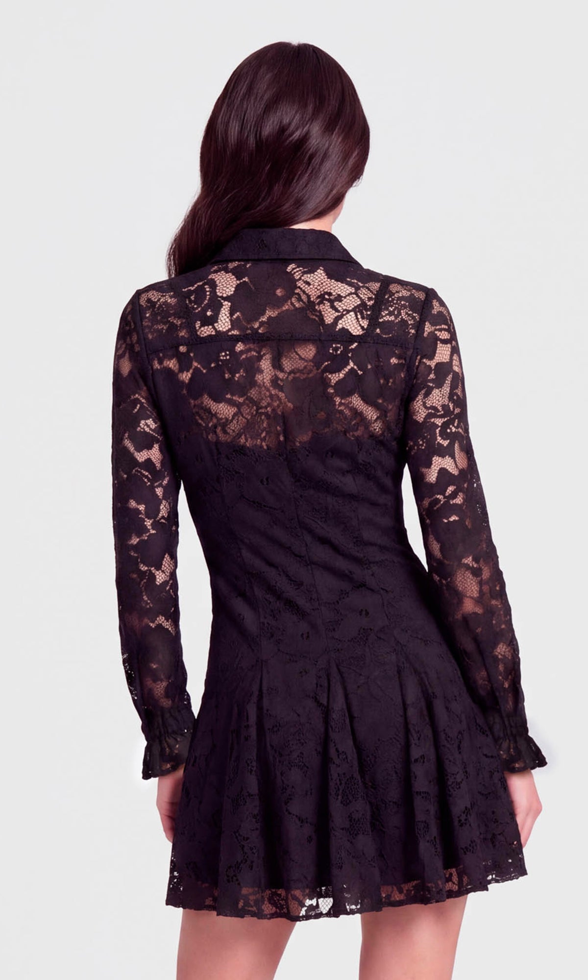 A woman shown from the back wearing a black lace long-sleeve mini dress with a pleated skirt.