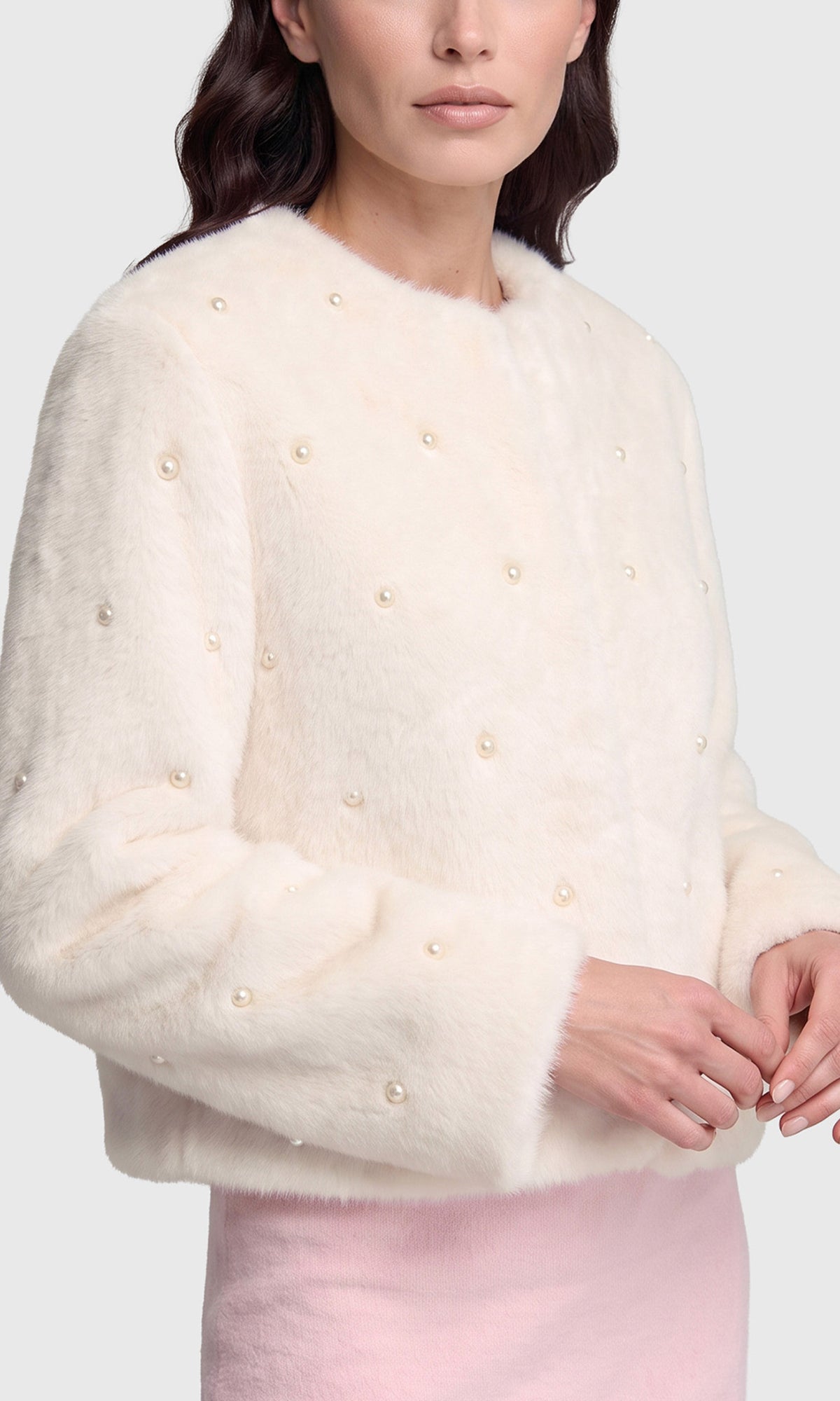 A close-up of a model wearing a cream faux fur cropped sweater decorated with small pearl embellishments.