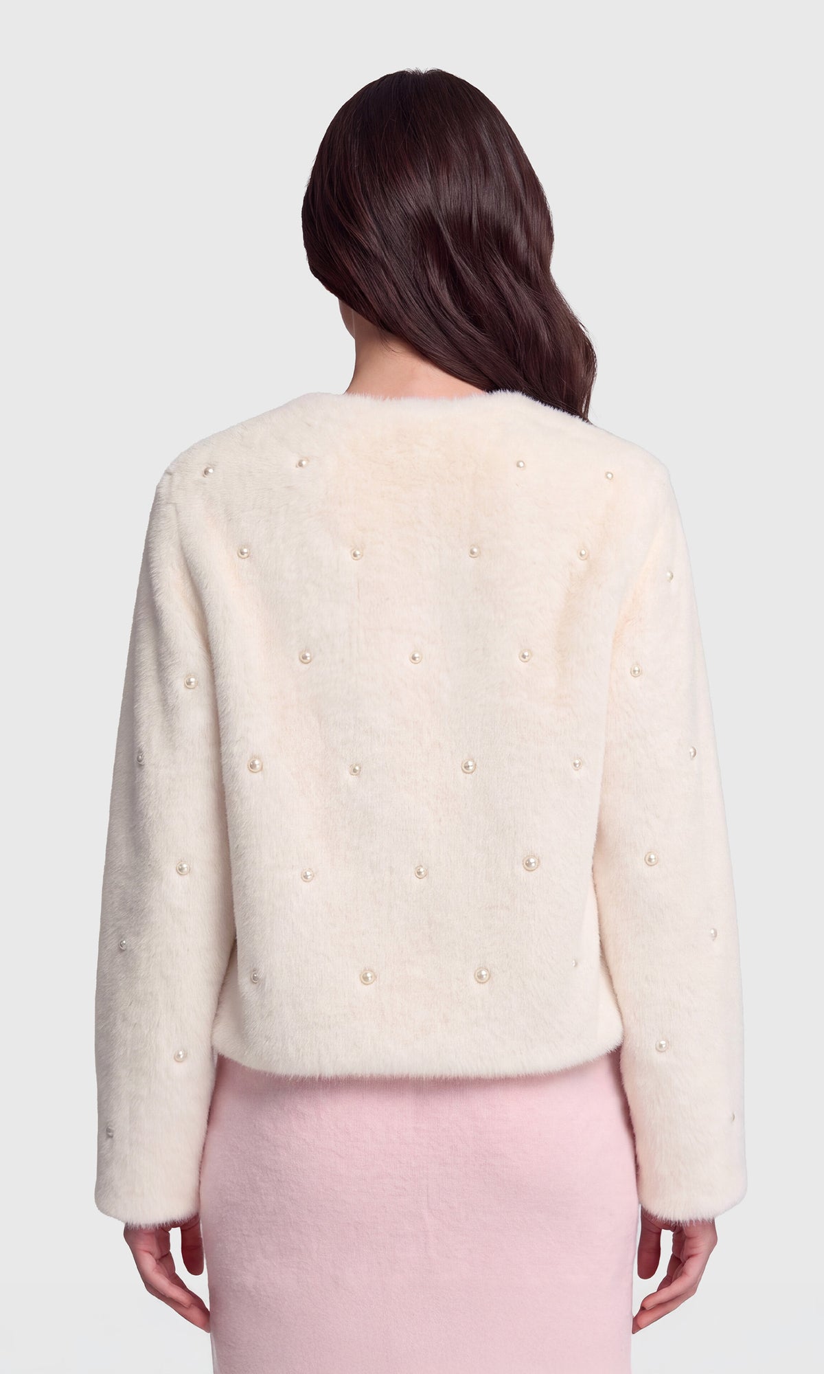 A woman shown from the back wearing a cream-colored fuzzy cropped sweater with small pearl embellishments and a light pink dress.