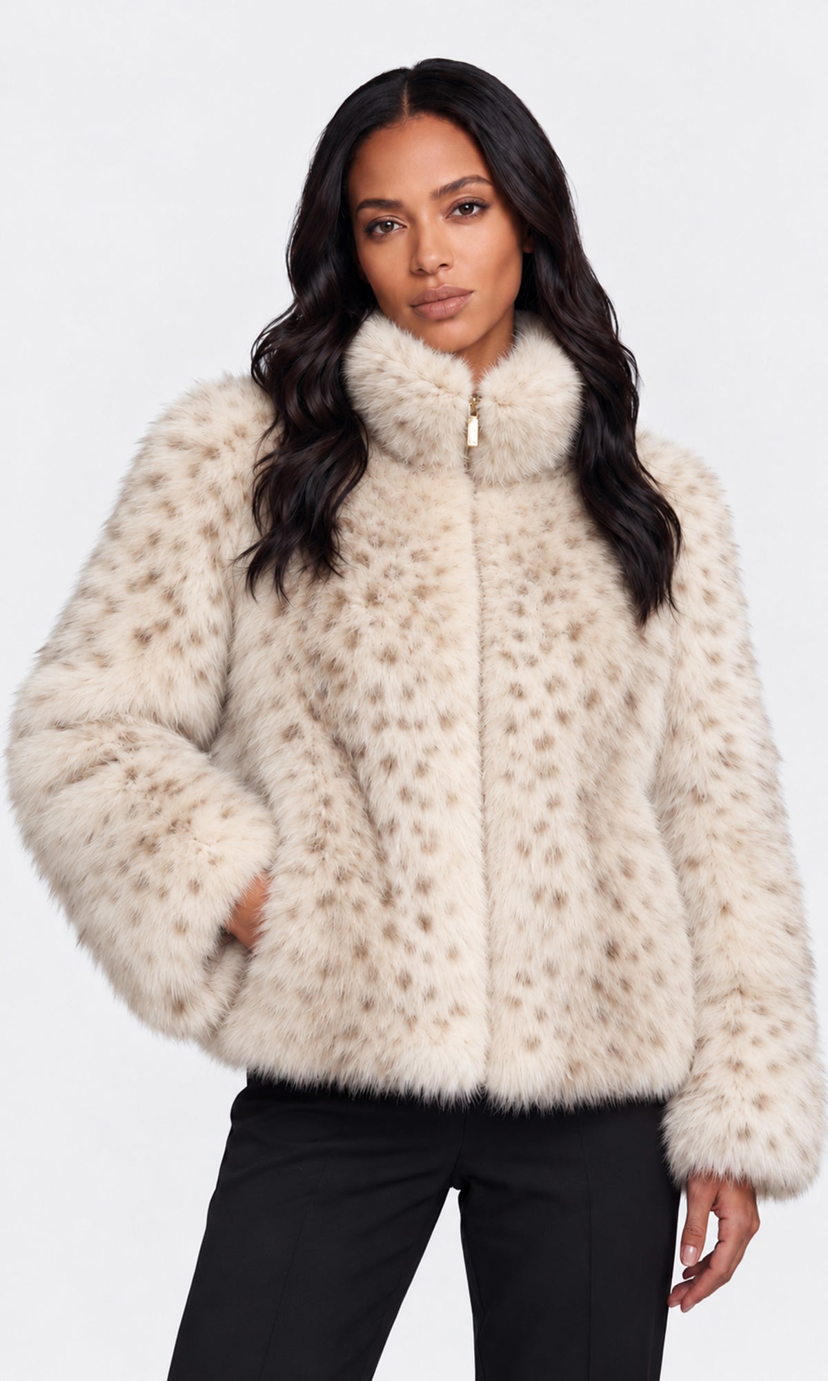 A woman modeling a cream faux fur jacket with a subtle tan leopard print pattern, high collar, and front zipper, paired with black pants.
