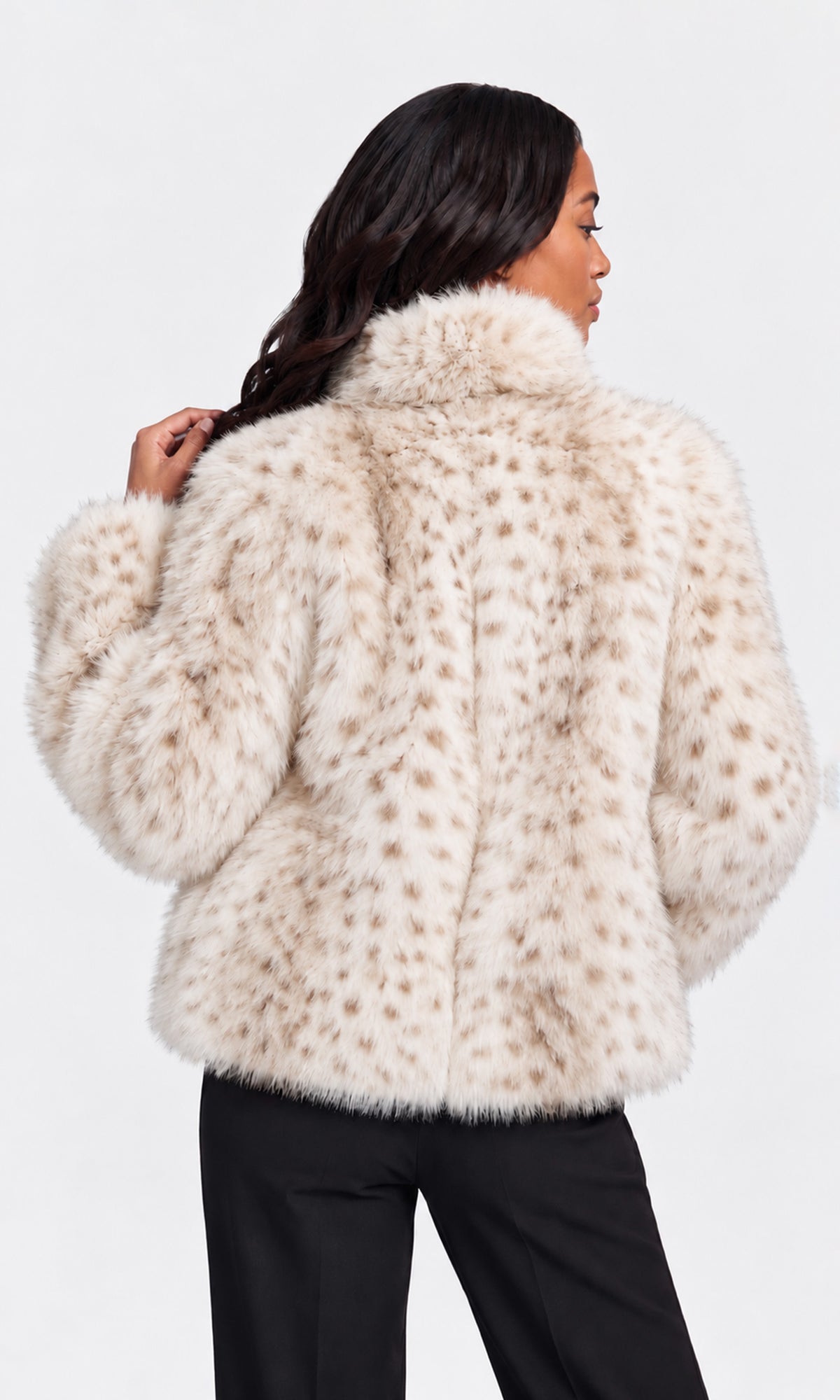 A woman shown from the back wearing a cream faux fur jacket with brown spots, paired with black pants.