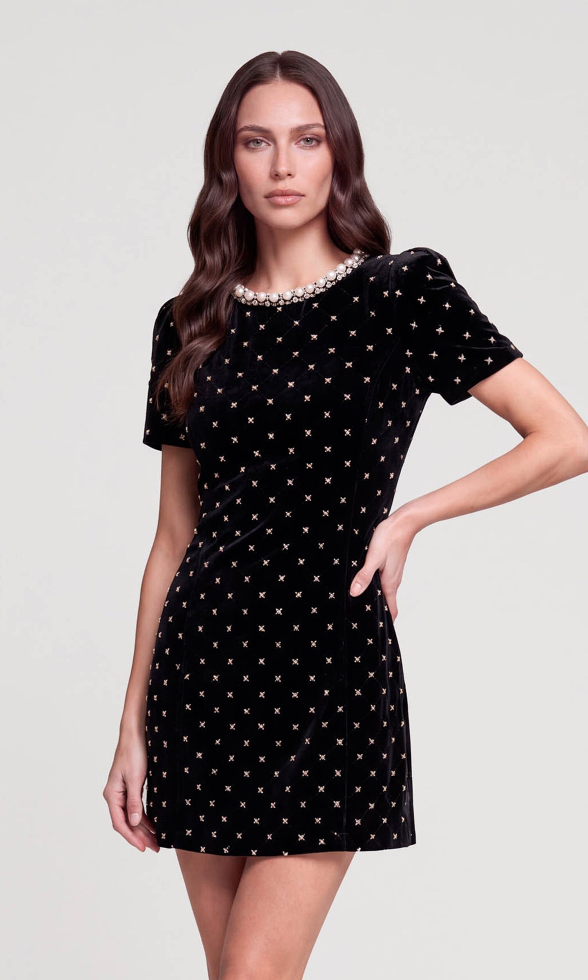 A woman modeling a short-sleeved black velvet dress with a white geometric pattern and a pearl-trimmed neckline.