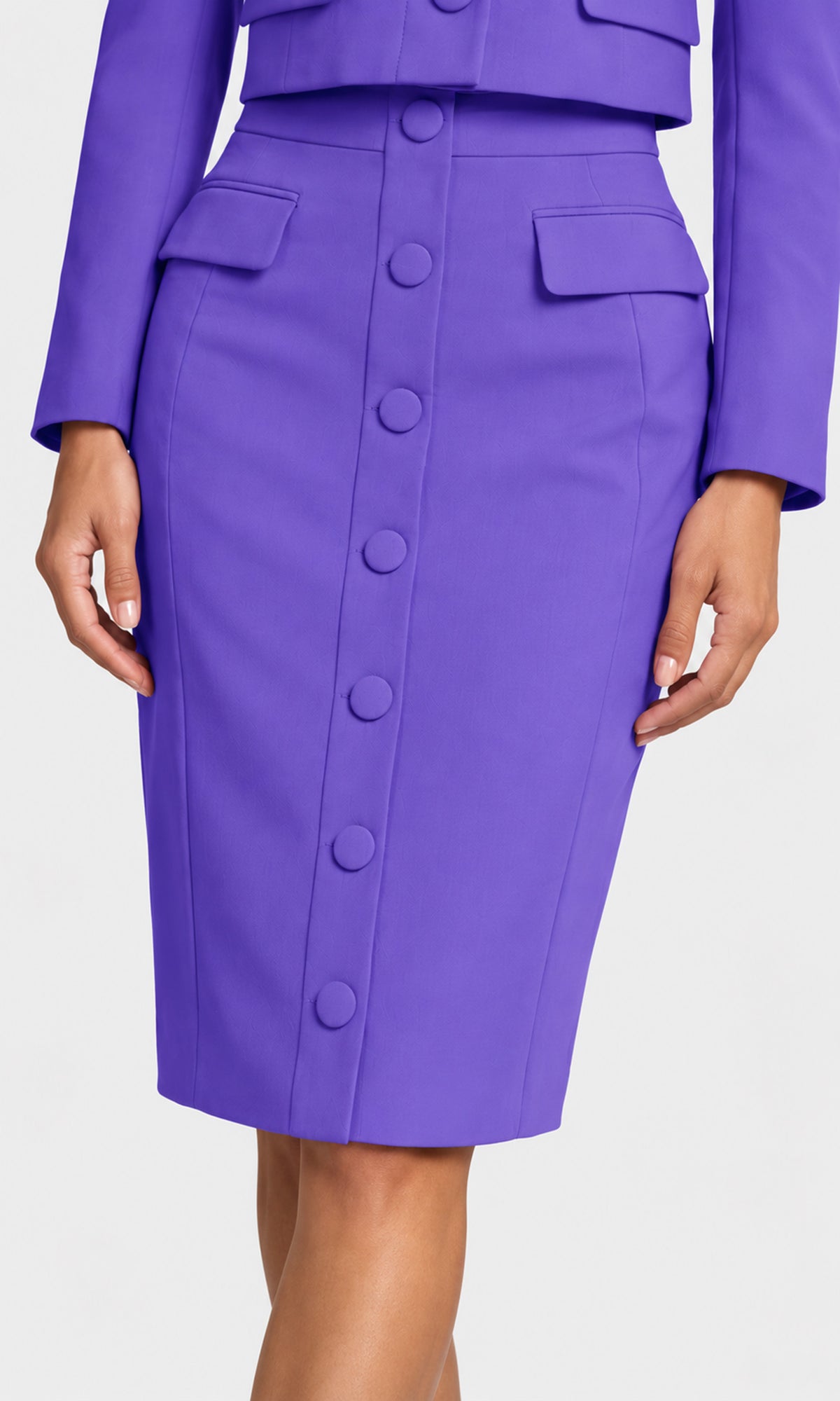 A close-up of a model wearing a vibrant purple knee-length pencil skirt with a button-down front and matching buttoned flap pockets, paired with a matching purple blazer.