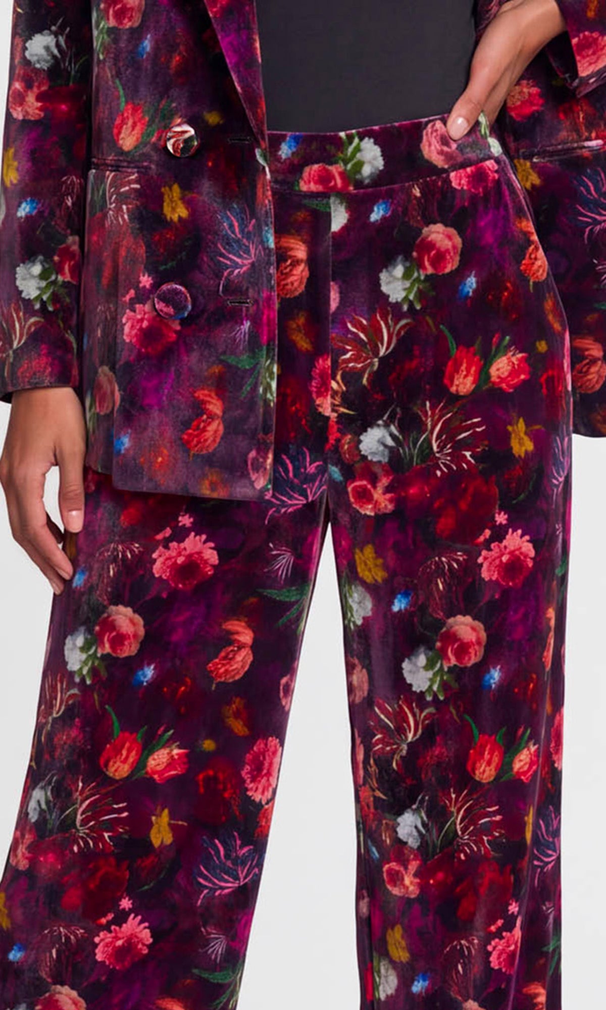 A close-up of a person wearing a matching velvet blazer and trousers set in a deep purple fabric with a dense multicolor floral print.